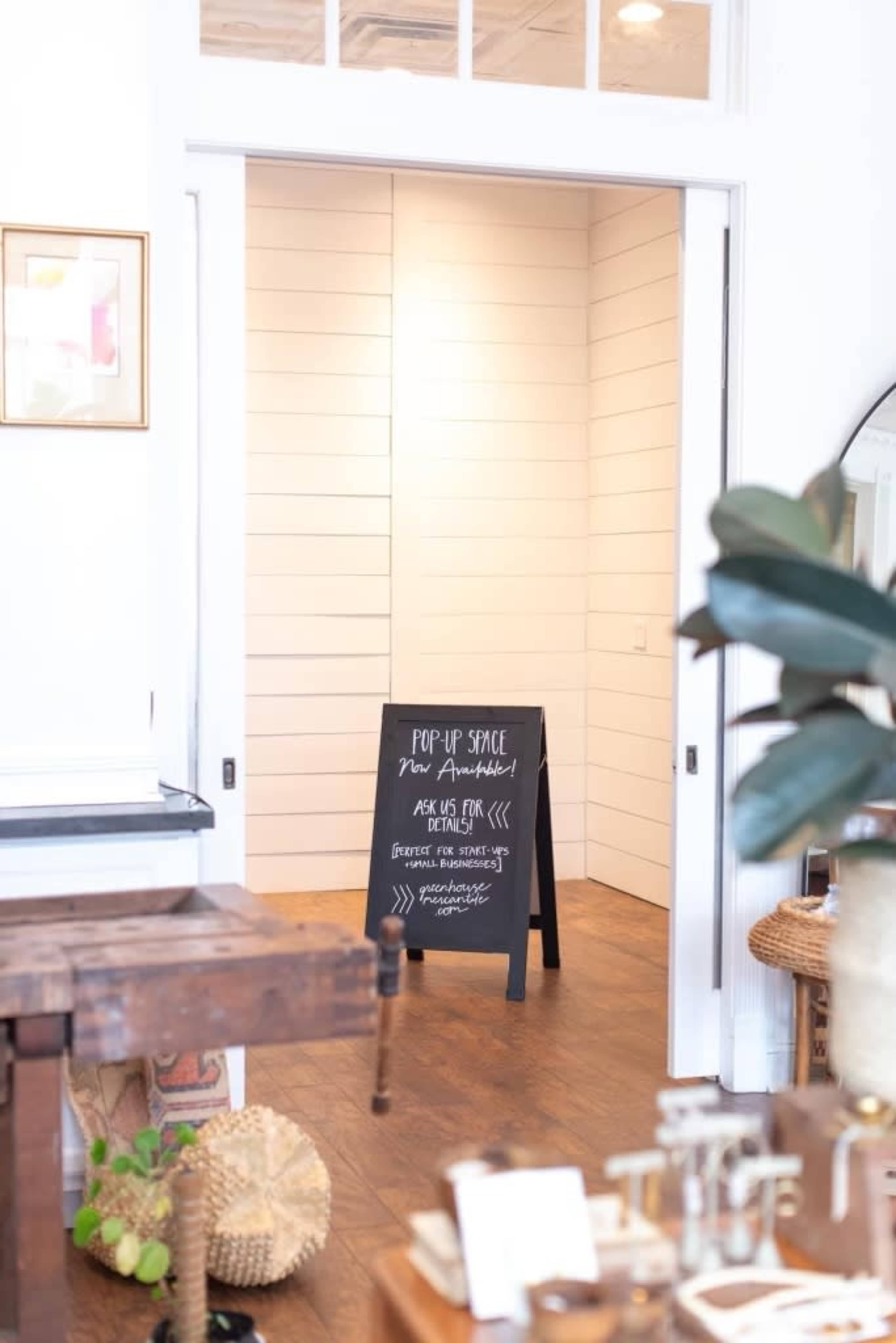 A pop-up space sign stands on a wooden floor in front of a light-colored room with white shiplap walls.
