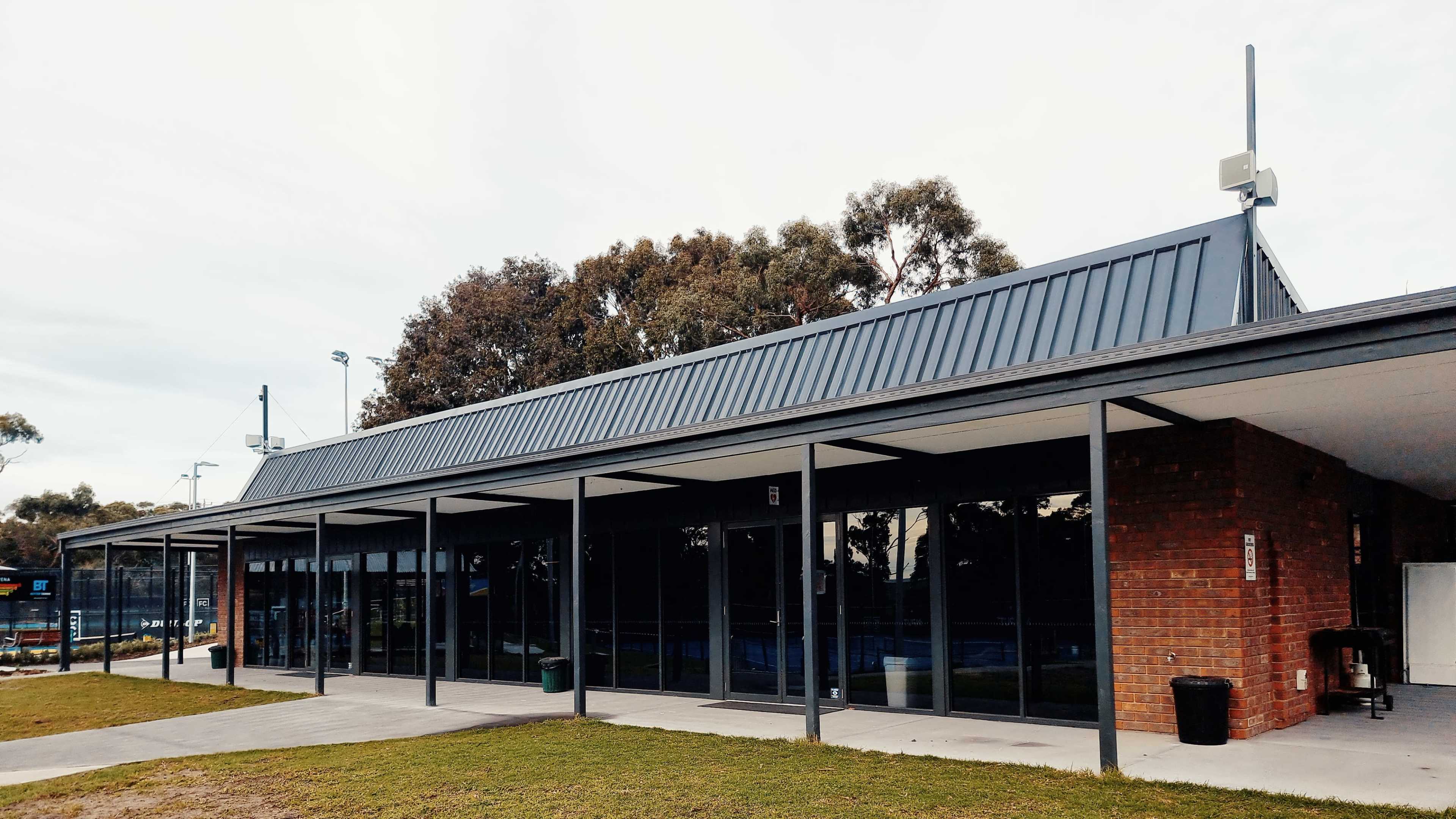 A modern single-story building with a flat roof, large glass windows, and a brick facade, set in a grassy area with a sports court nearby.