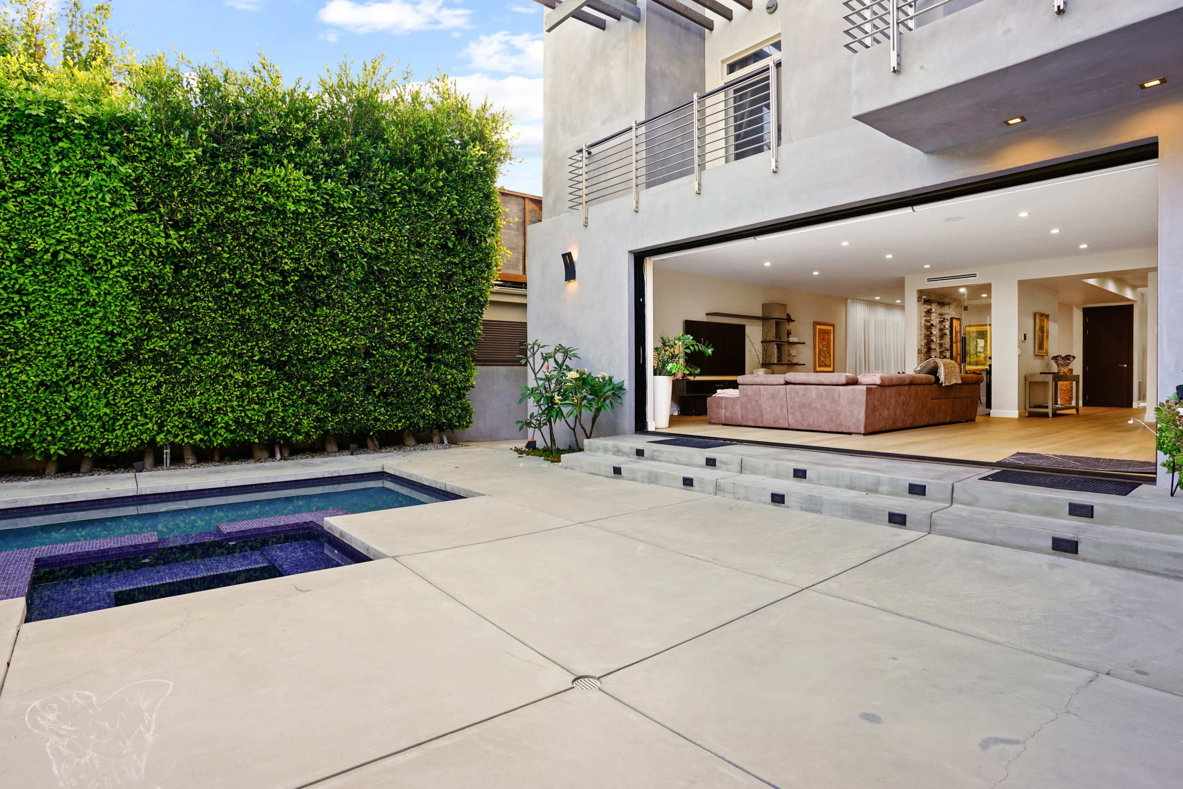 A modern backyard features a pool and a spacious patio leading to an open-concept living area with large sliding doors.
