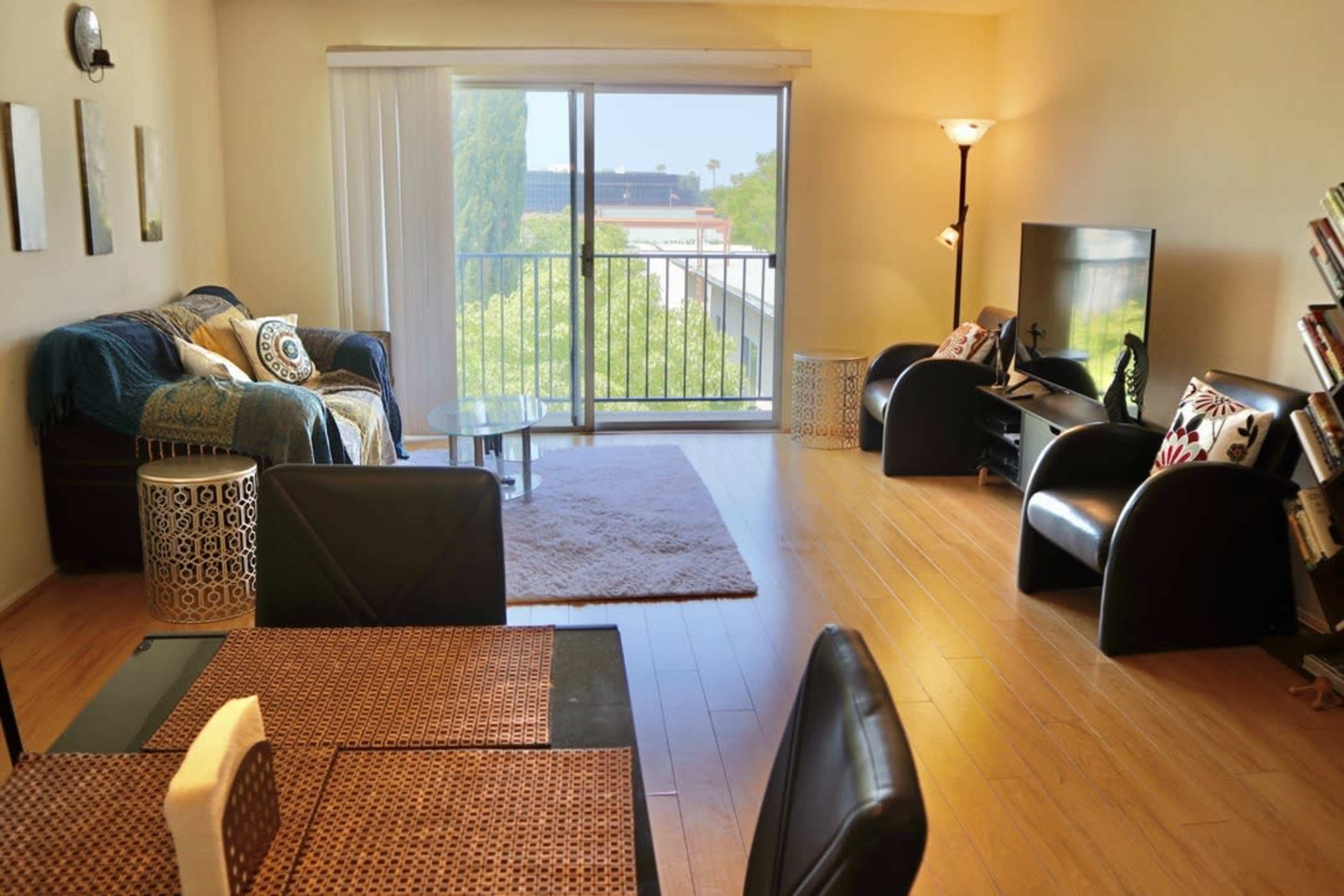 A modern living room with a large window, a couch and chairs, a glass coffee table, and a television.