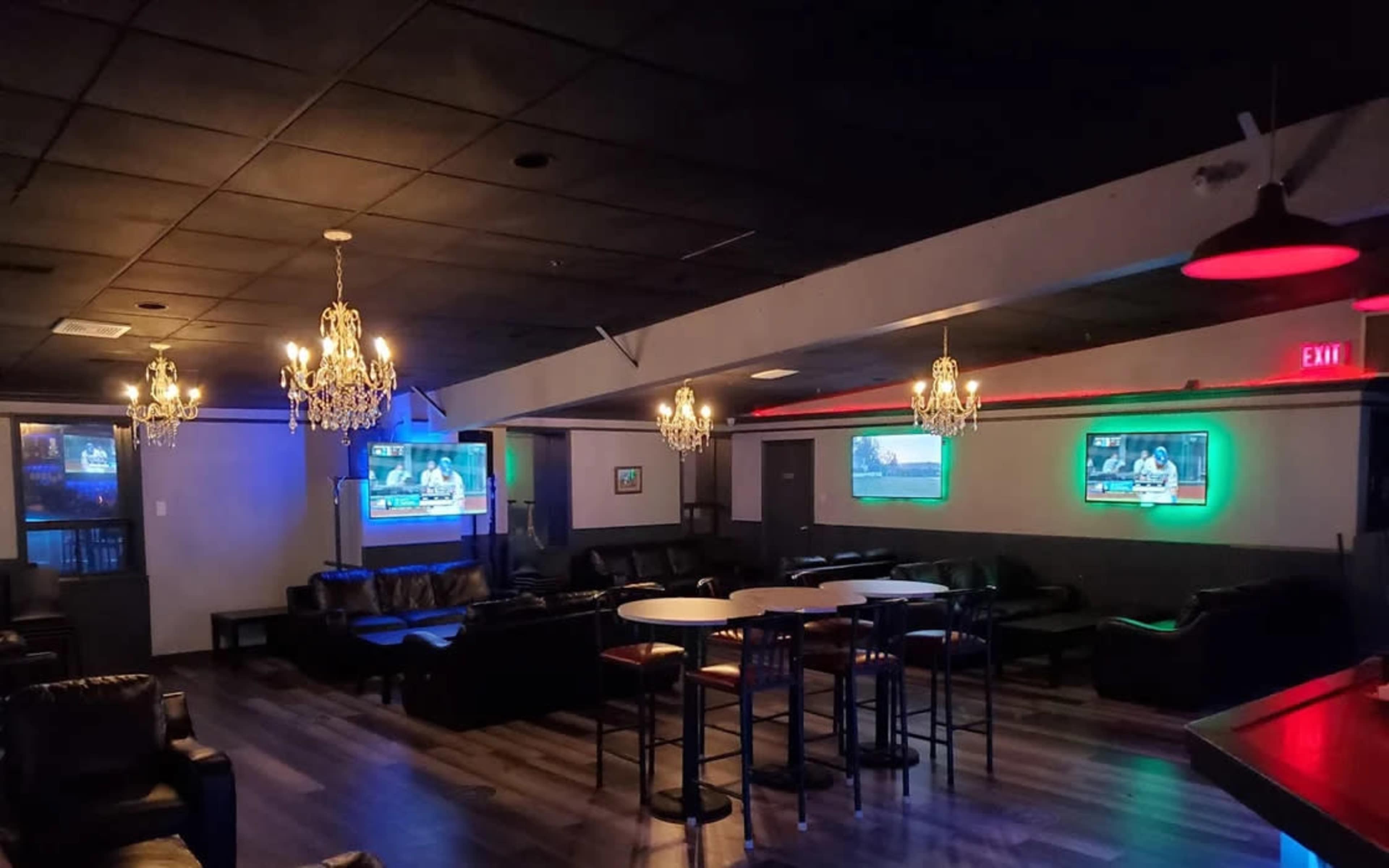 A spacious lounge area with leather seating, illuminated by chandeliers, and featuring multiple screens displaying television content on the walls.