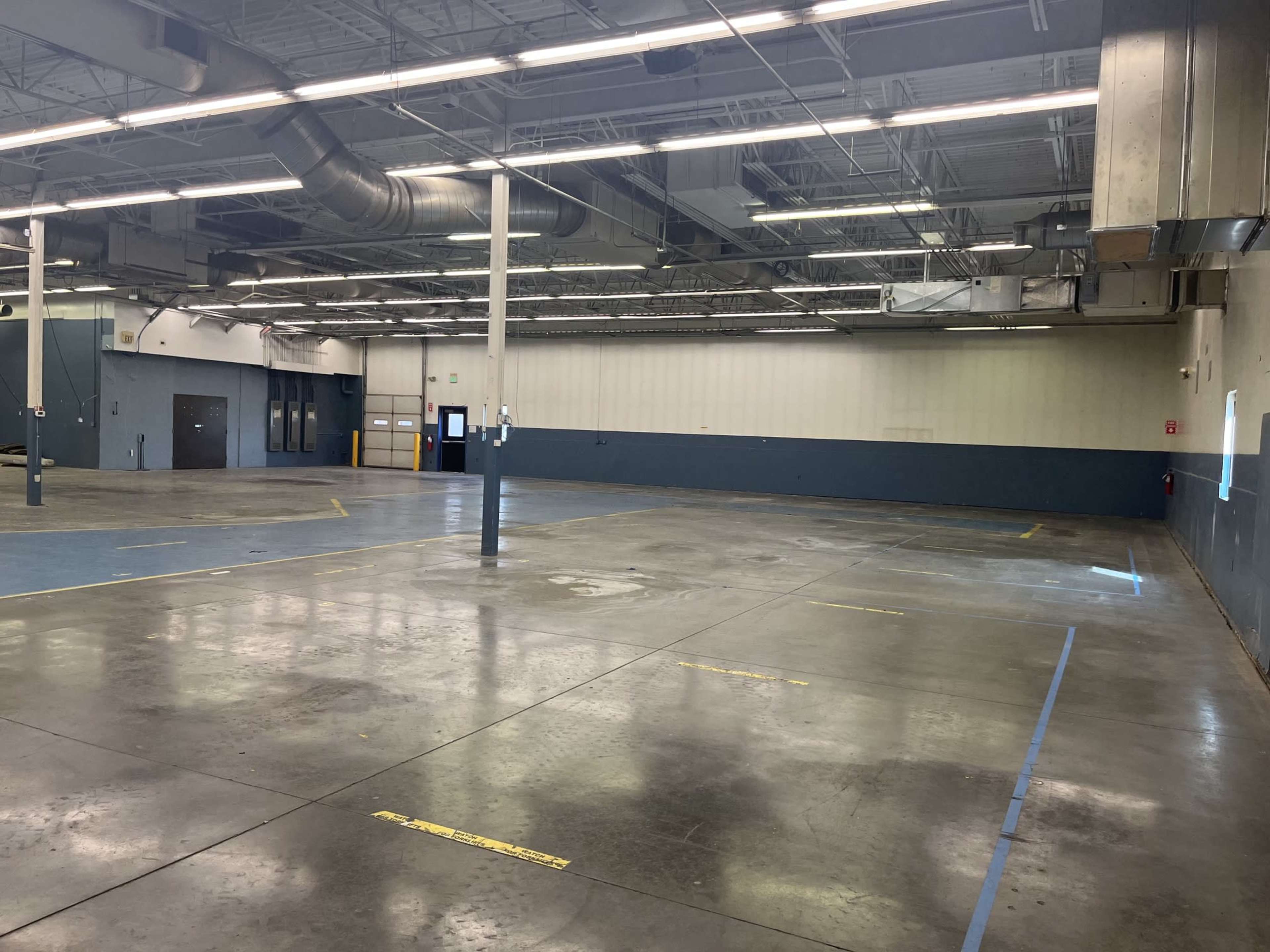 The image shows an empty industrial warehouse space with concrete flooring and a blue-painted wall.
