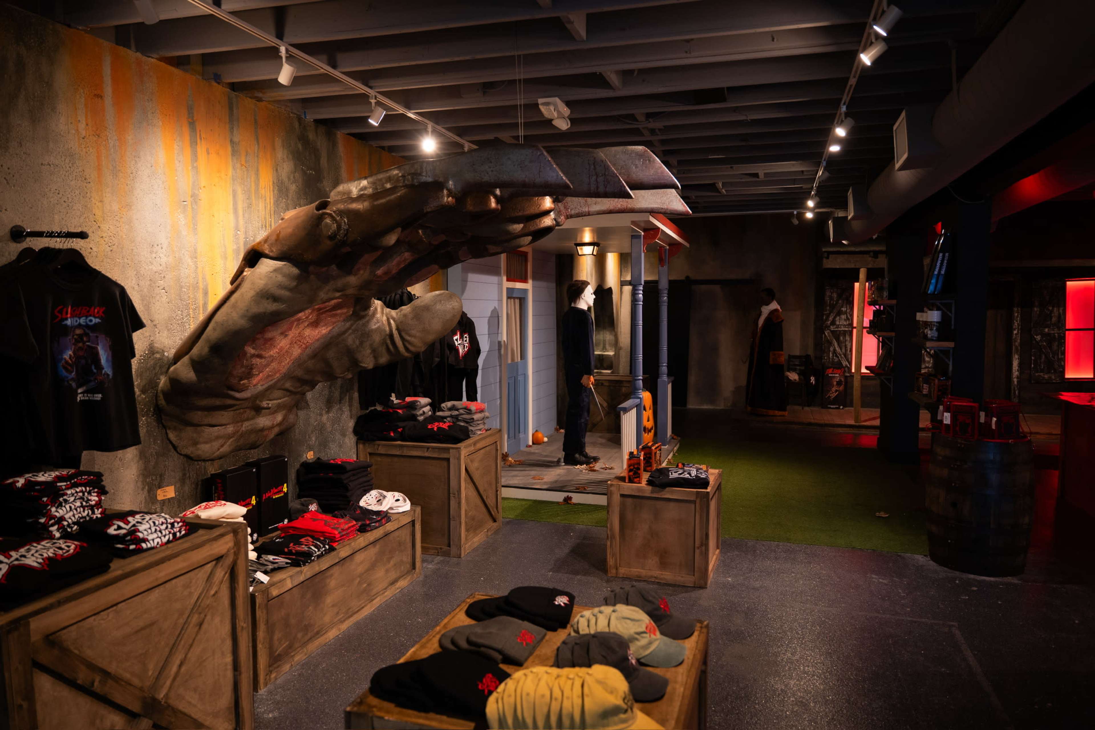 The image shows a retail store interior featuring various clothing items displayed on wooden structures, with an oversized claw sculpture protruding from the wall.