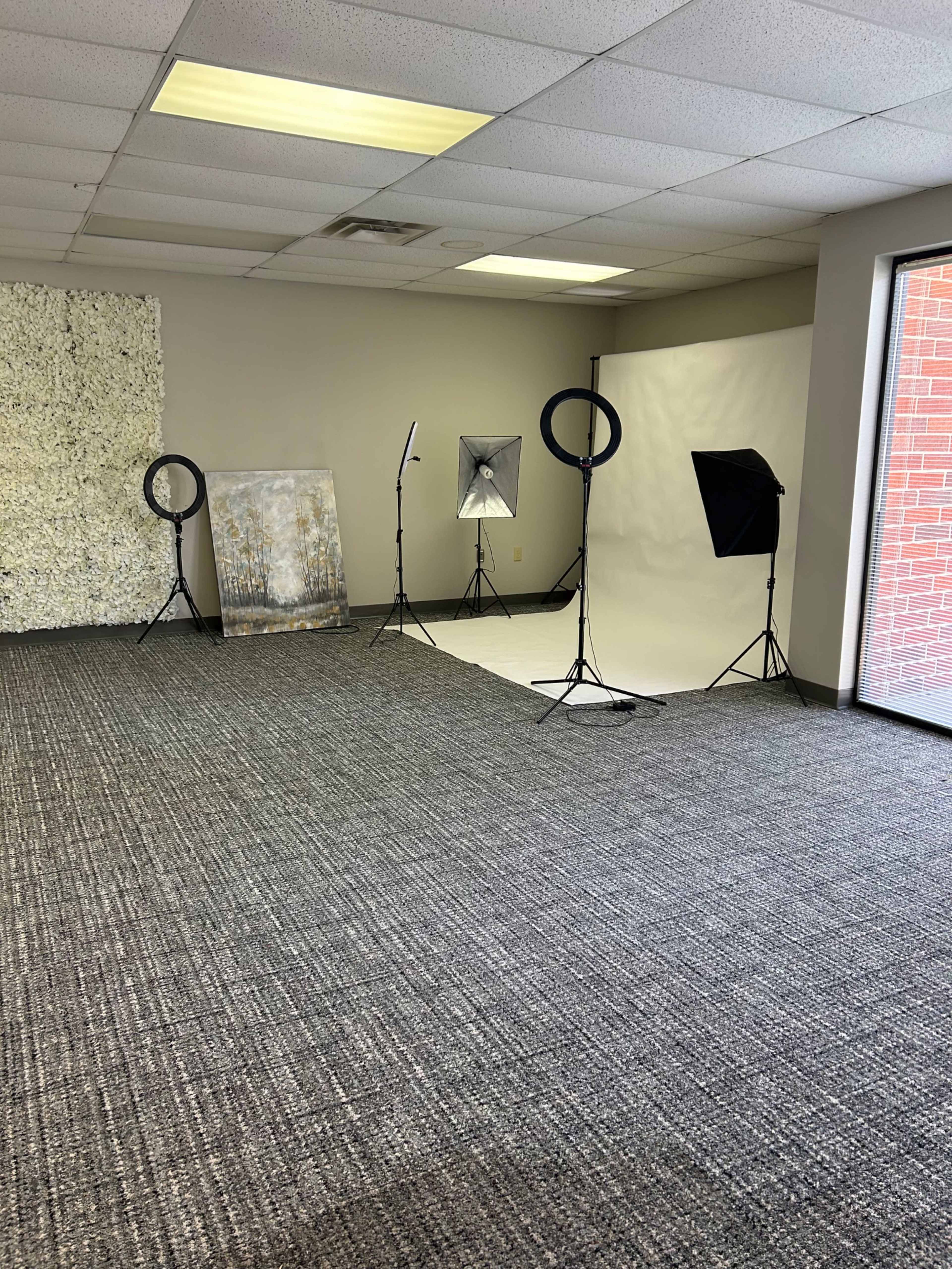 The image shows a spacious, empty room equipped with photography lighting setups and a backdrop.