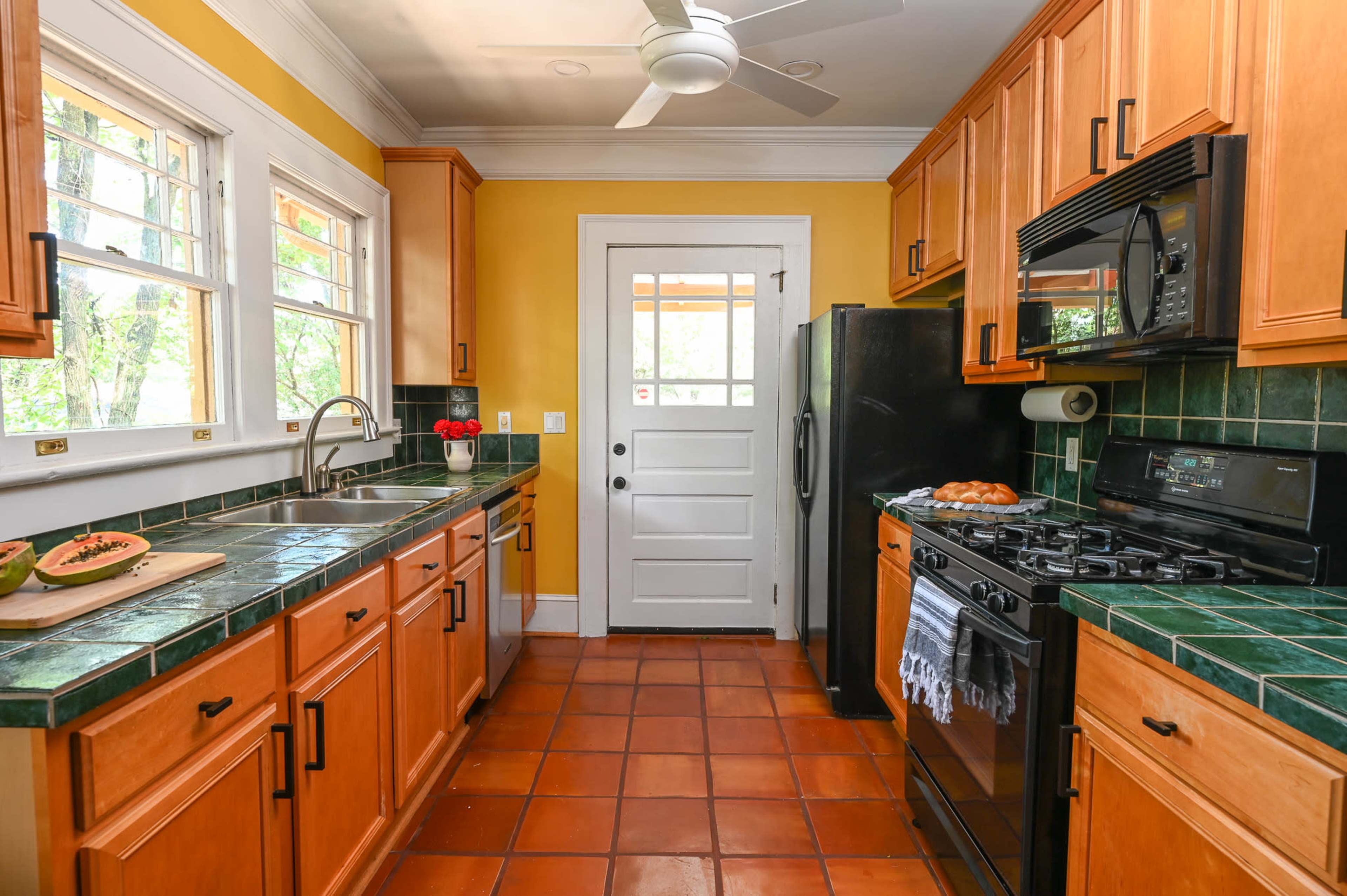 A kitchen with wooden cabinets, green tiled countertops, and a black stove and refrigerator.