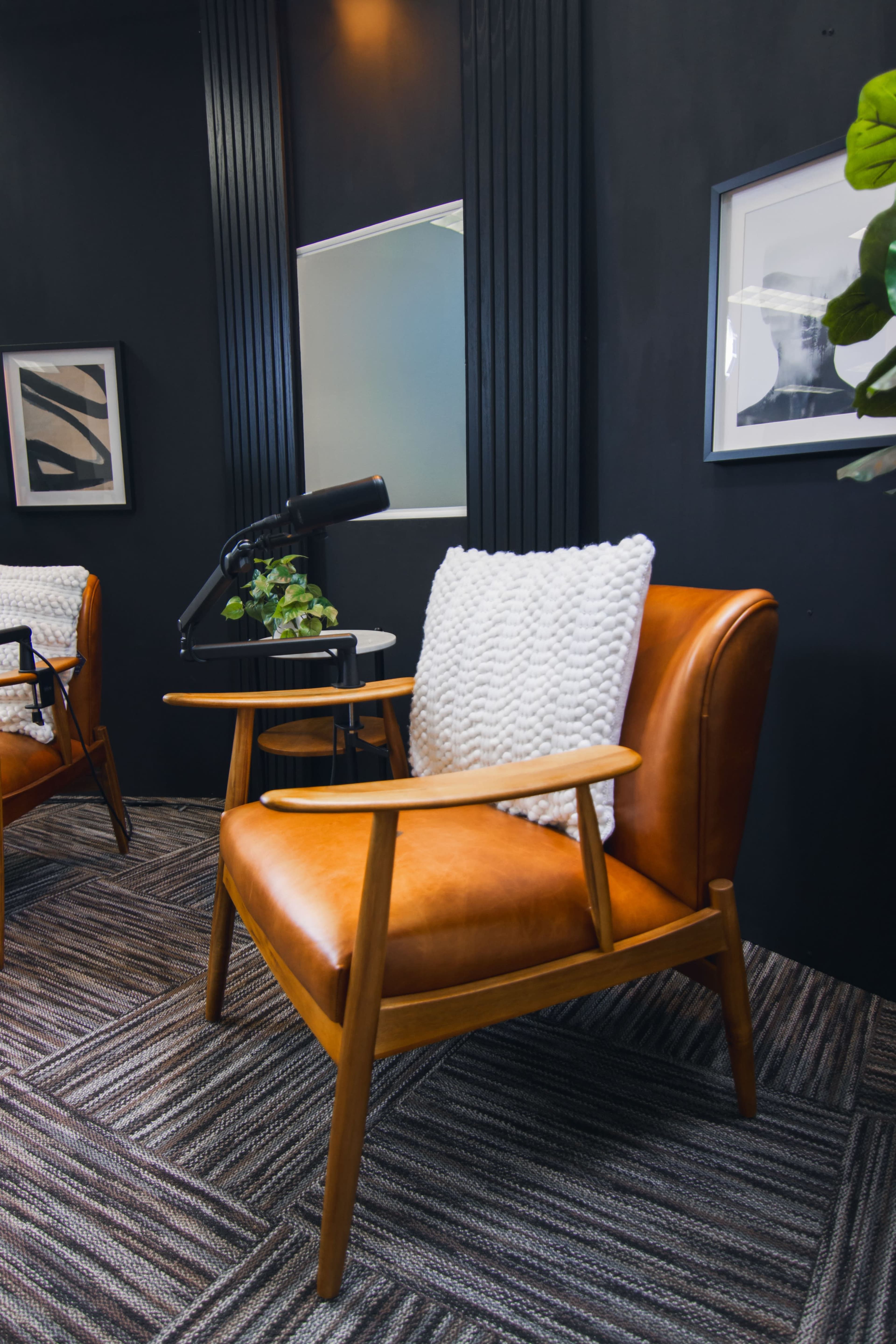 The image shows an inviting seating area featuring a brown leather armchair with a white pillow, a small round table, and decorative wall elements in a dark room.