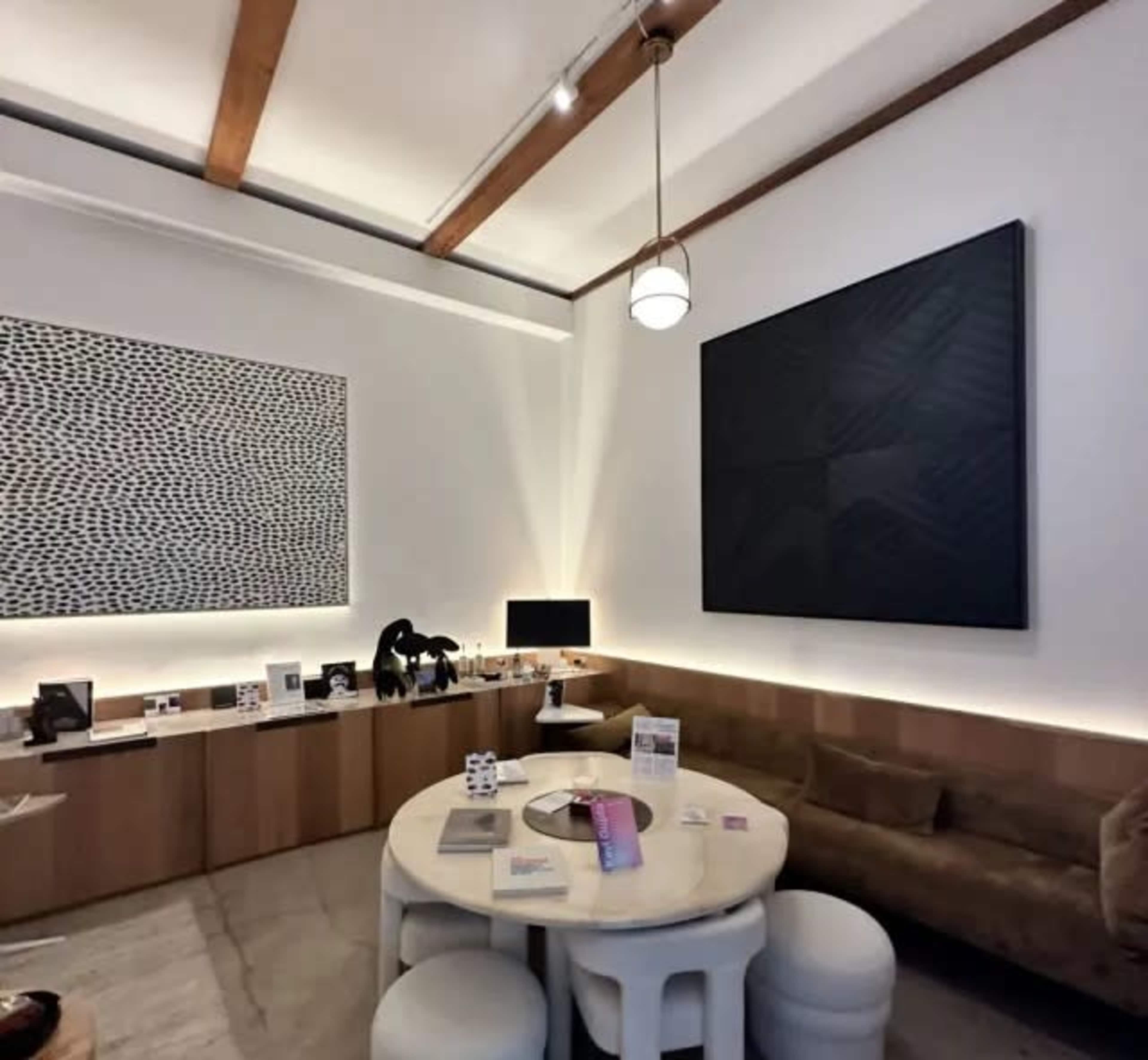 The image shows a modern interior space featuring a round white table, a plush sofa, and two abstract art pieces hanging on the walls.