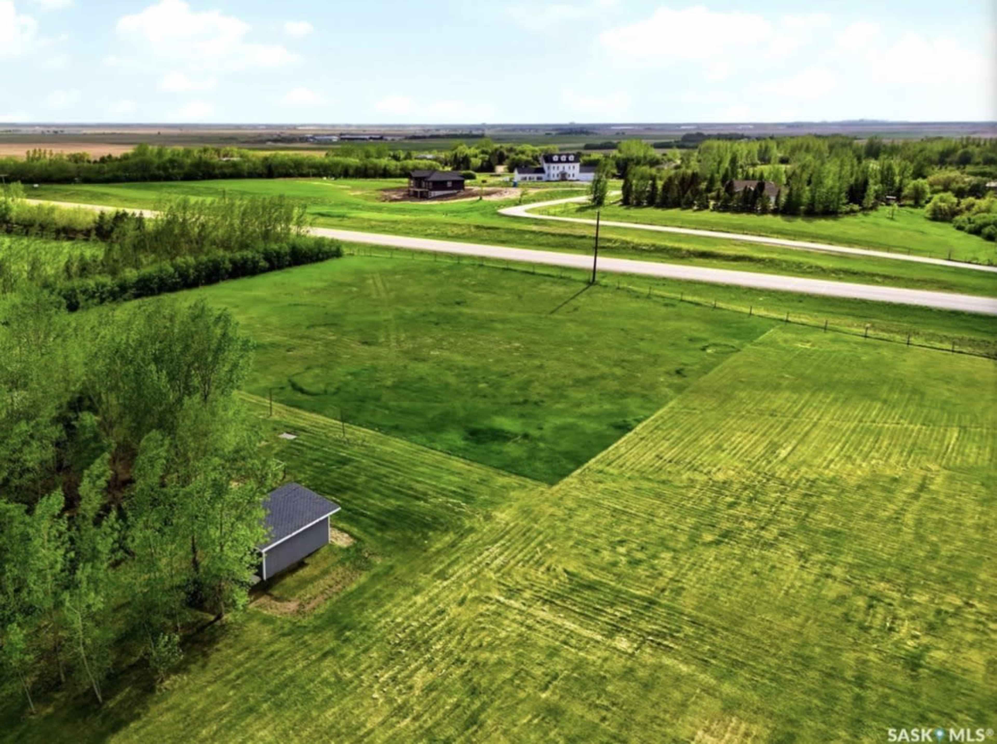 The image shows a green expanse of land with a few buildings, trees, and a road running alongside the property.