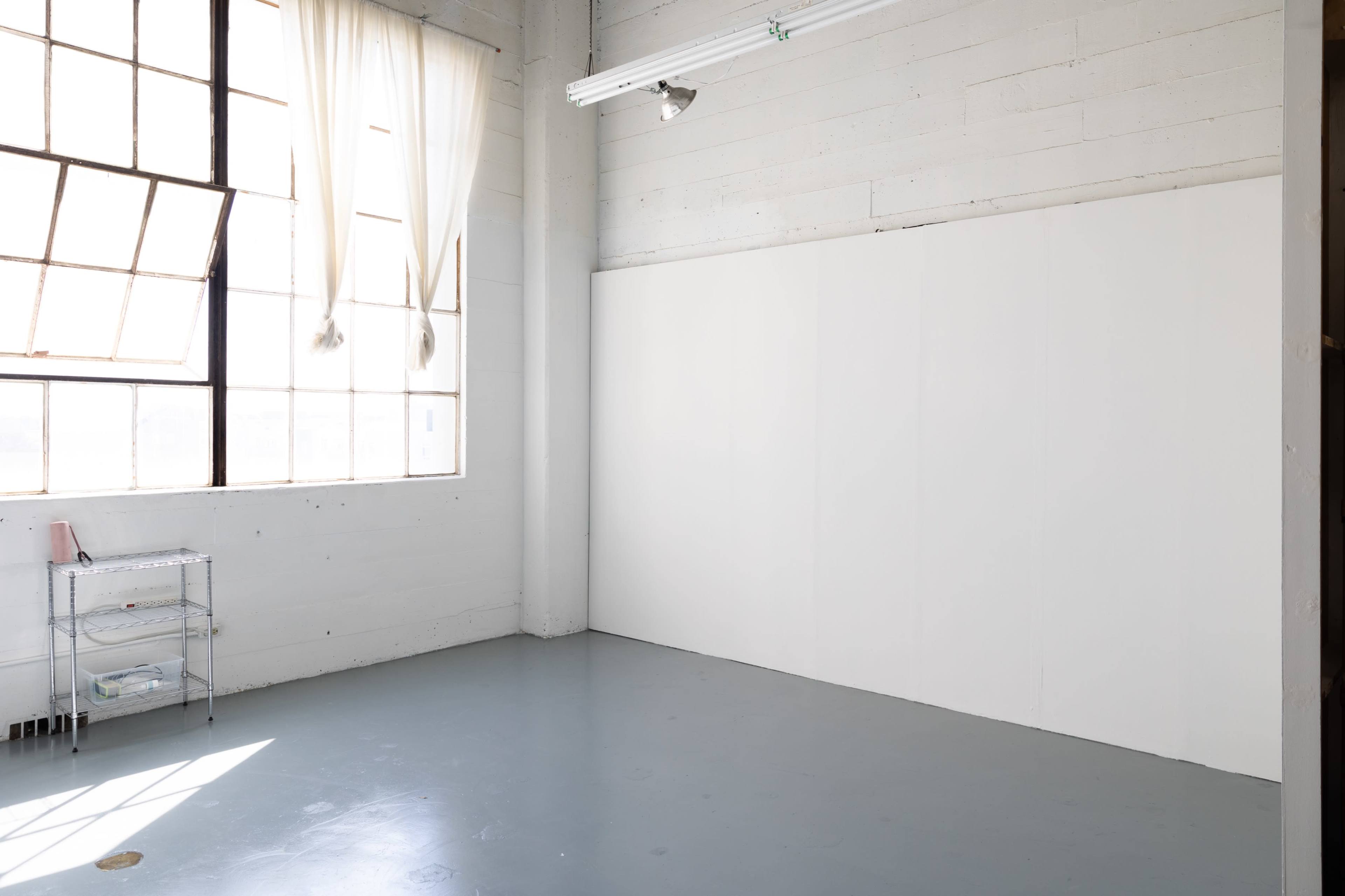 A well-lit, empty room with large windows and a blank white wall.