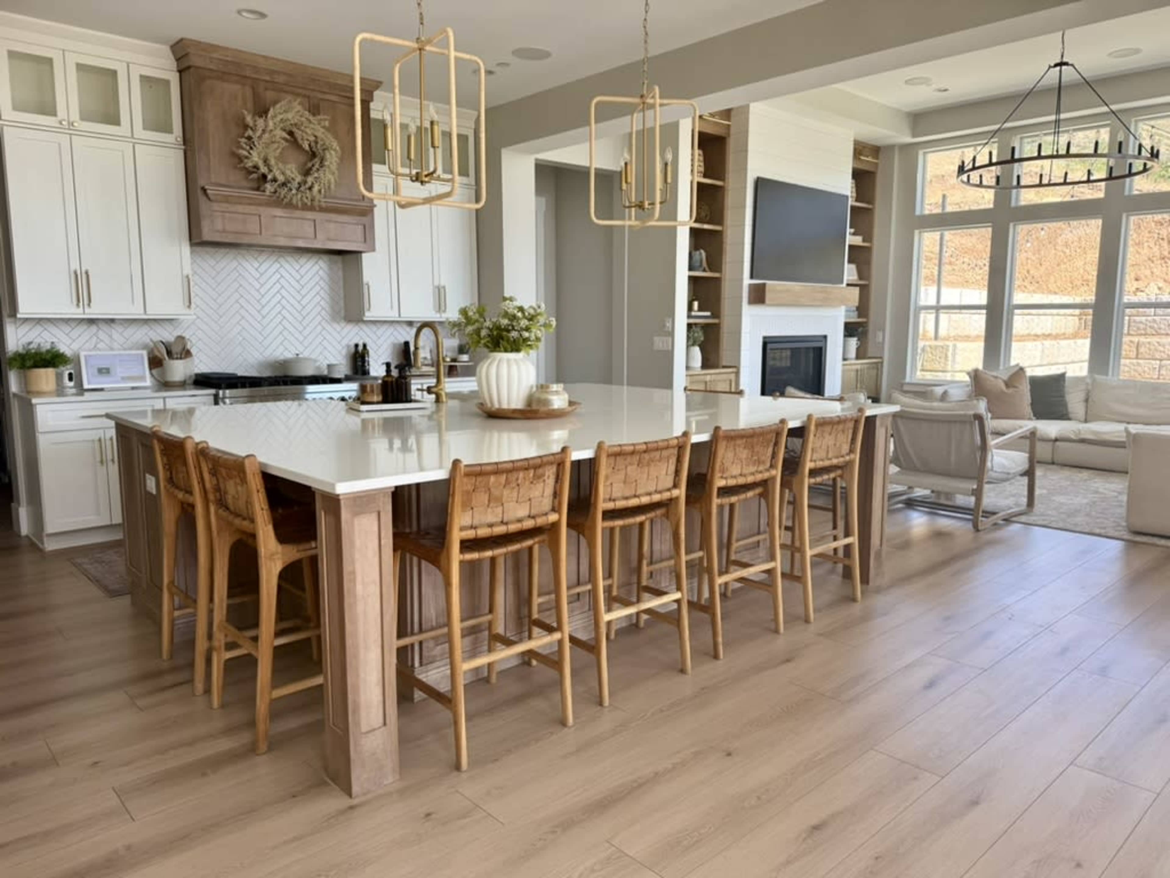 The image shows a modern kitchen with a large island and eight barstools, featuring white cabinets and a cozy seating area nearby.