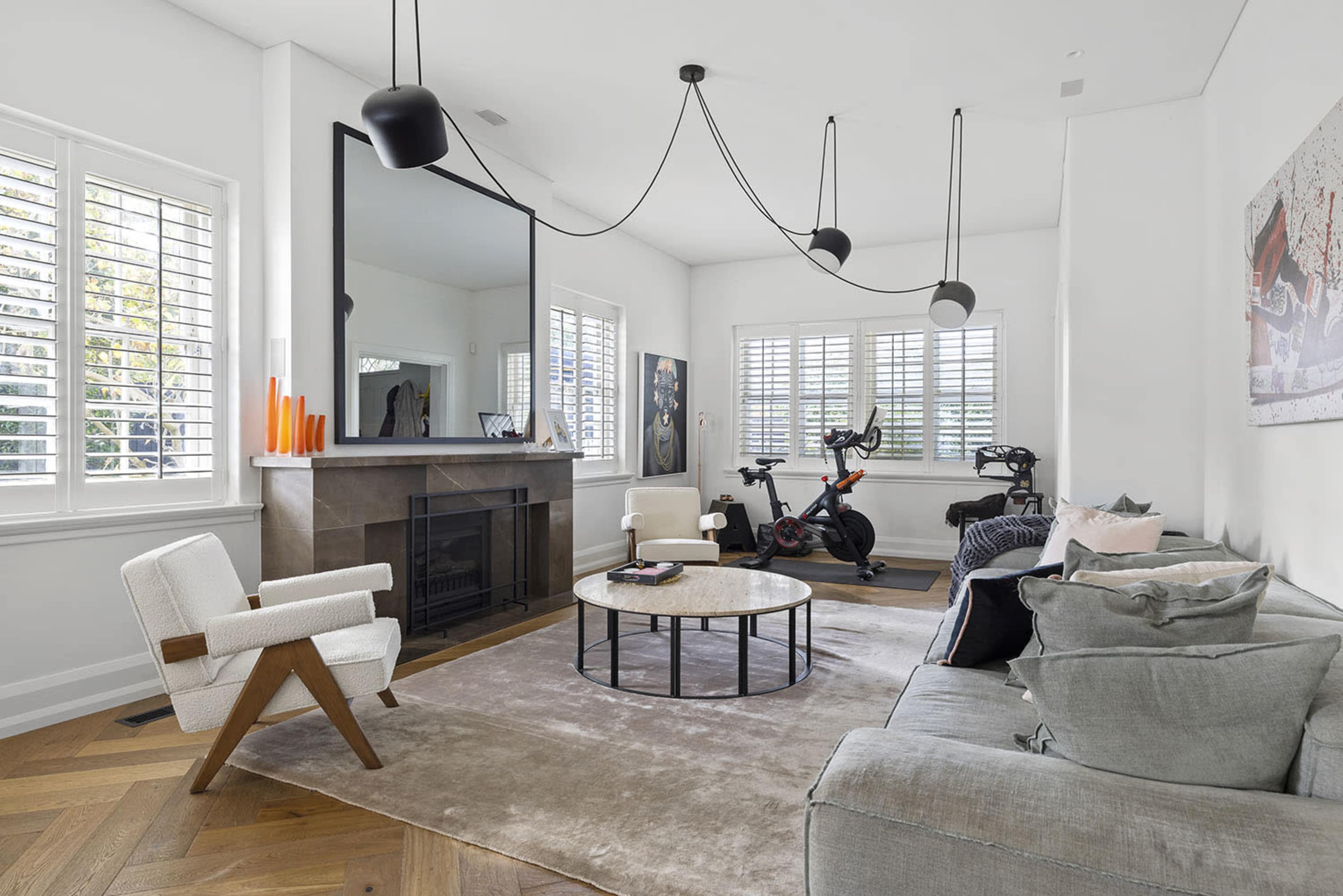 A modern living room featuring a large mirror, a circular coffee table, a sofa with various cushions, and a stationary bike beside a fireplace.