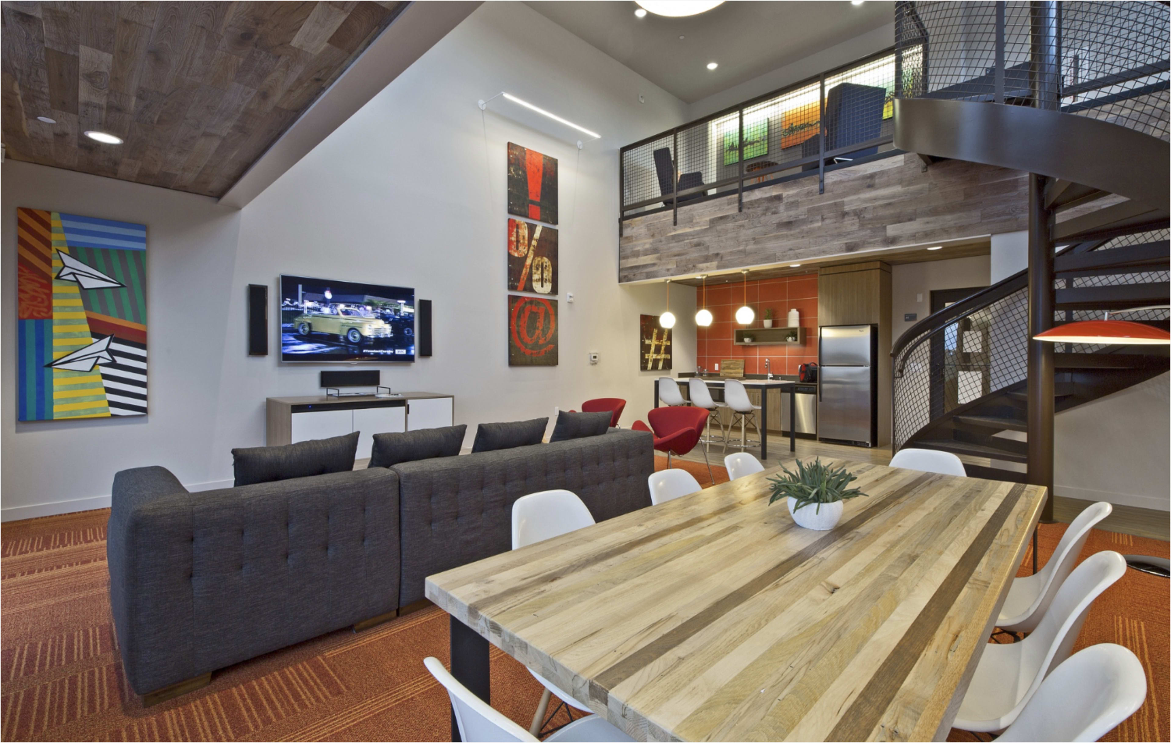 The image shows a modern living space featuring a sectional sofa, a wooden dining table, a television mounted on the wall, and a spiral staircase leading to a loft area.