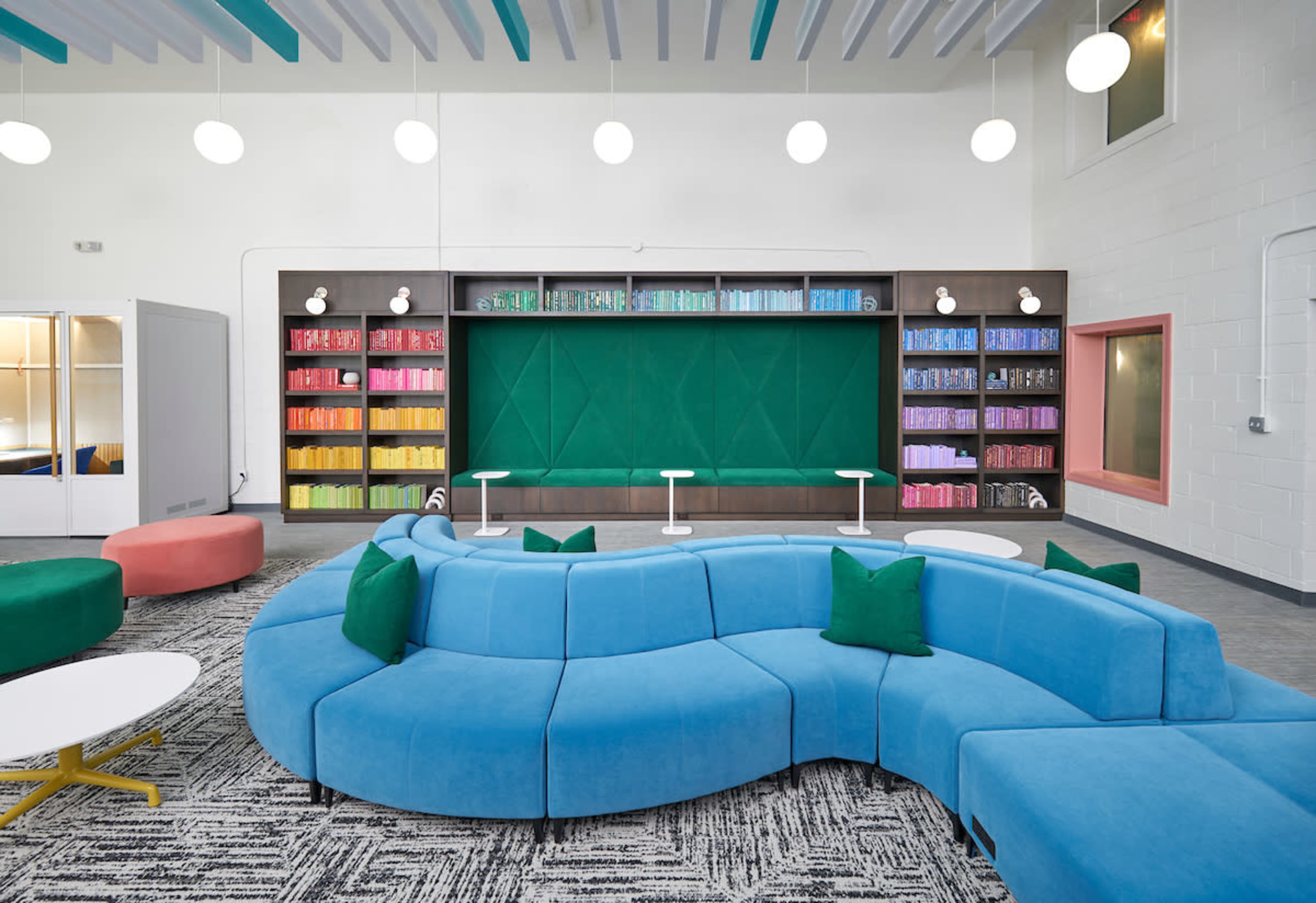 A modern room features a curved blue seating arrangement, colorful bookshelves, and bright overhead lighting.