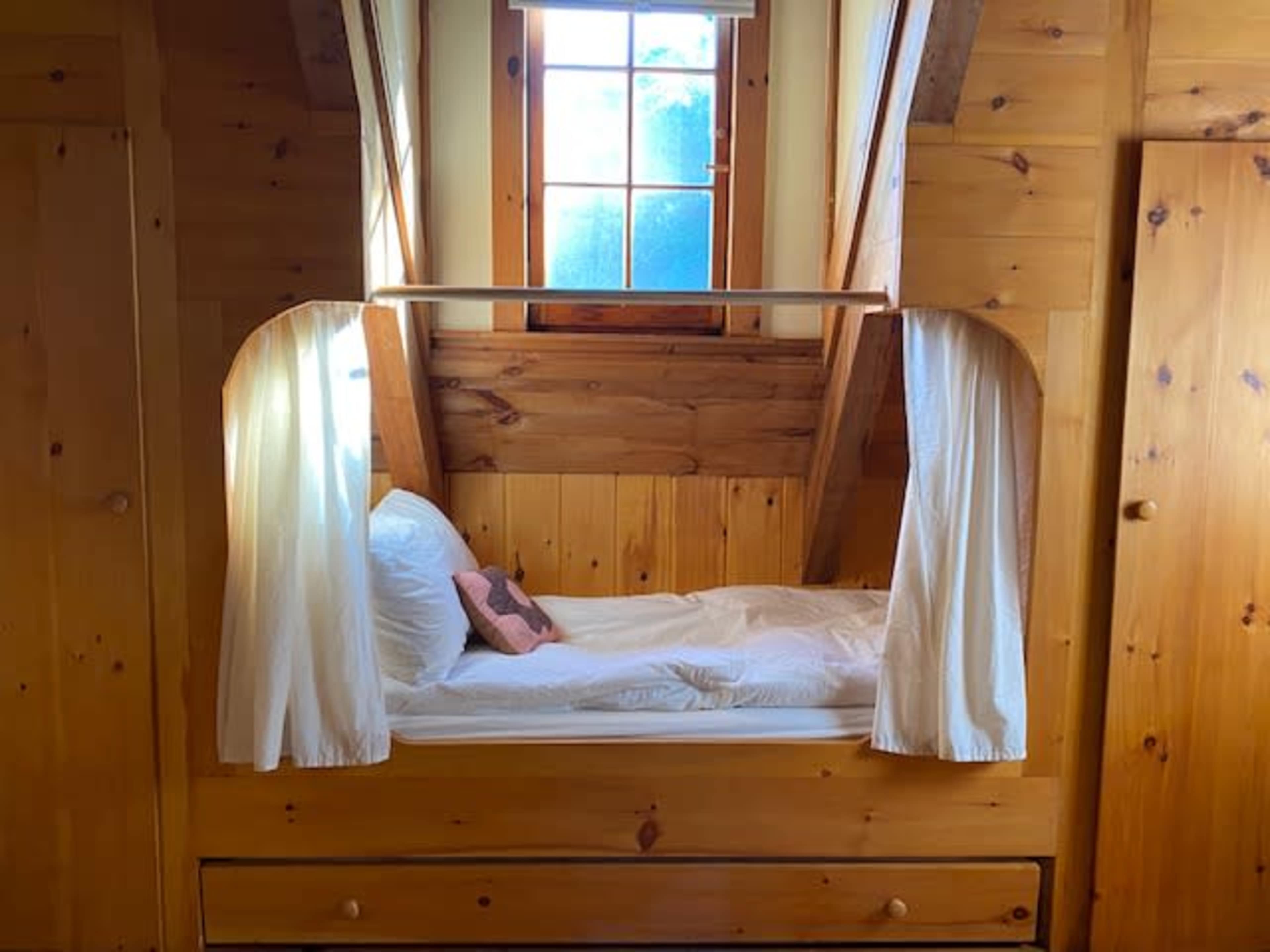 A small wooden bedroom with a cozy bed framed by slanted walls and a window letting in natural light.