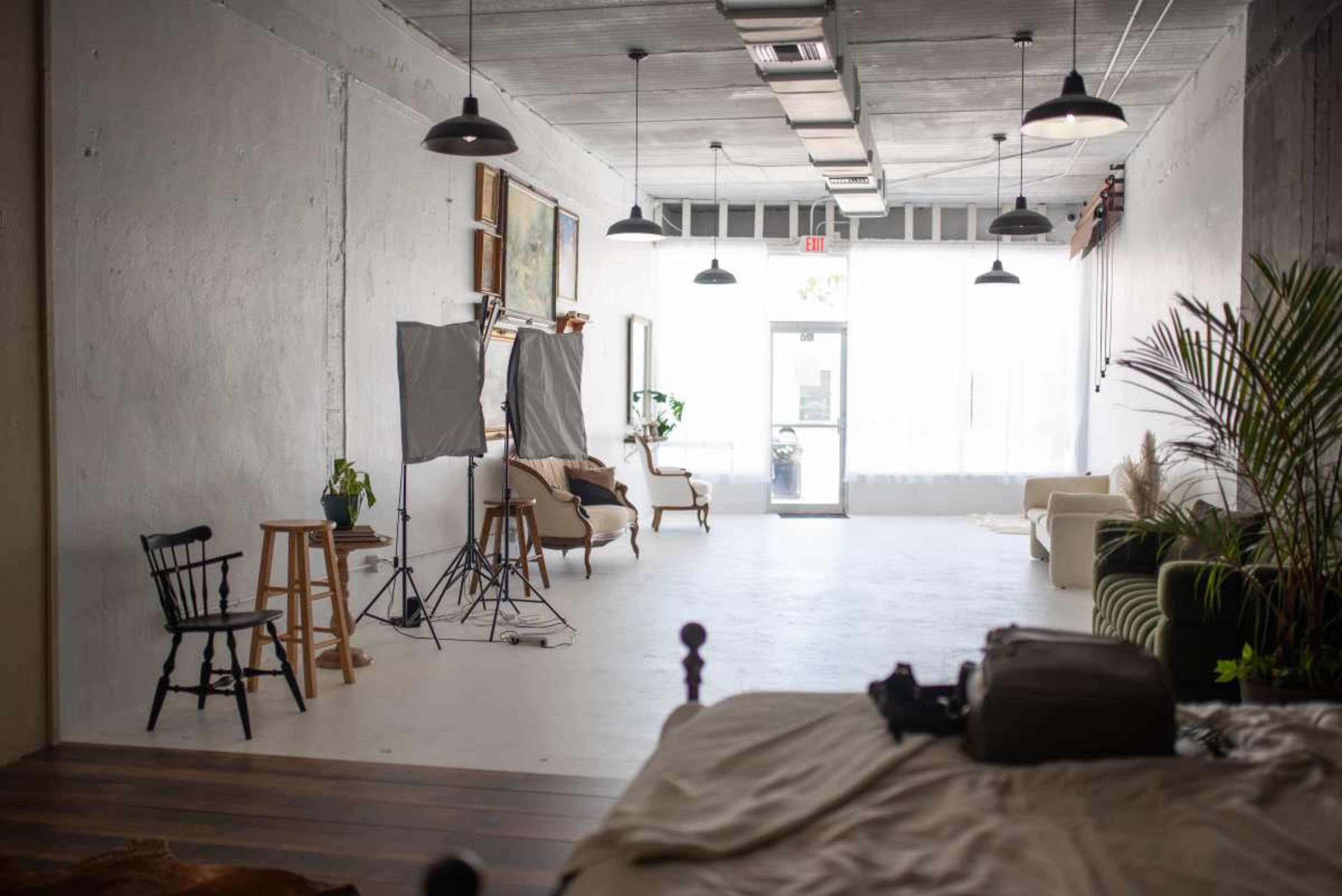 A spacious, well-lit room featuring simple furniture, including a sofa and a chair, along with a photography setup.