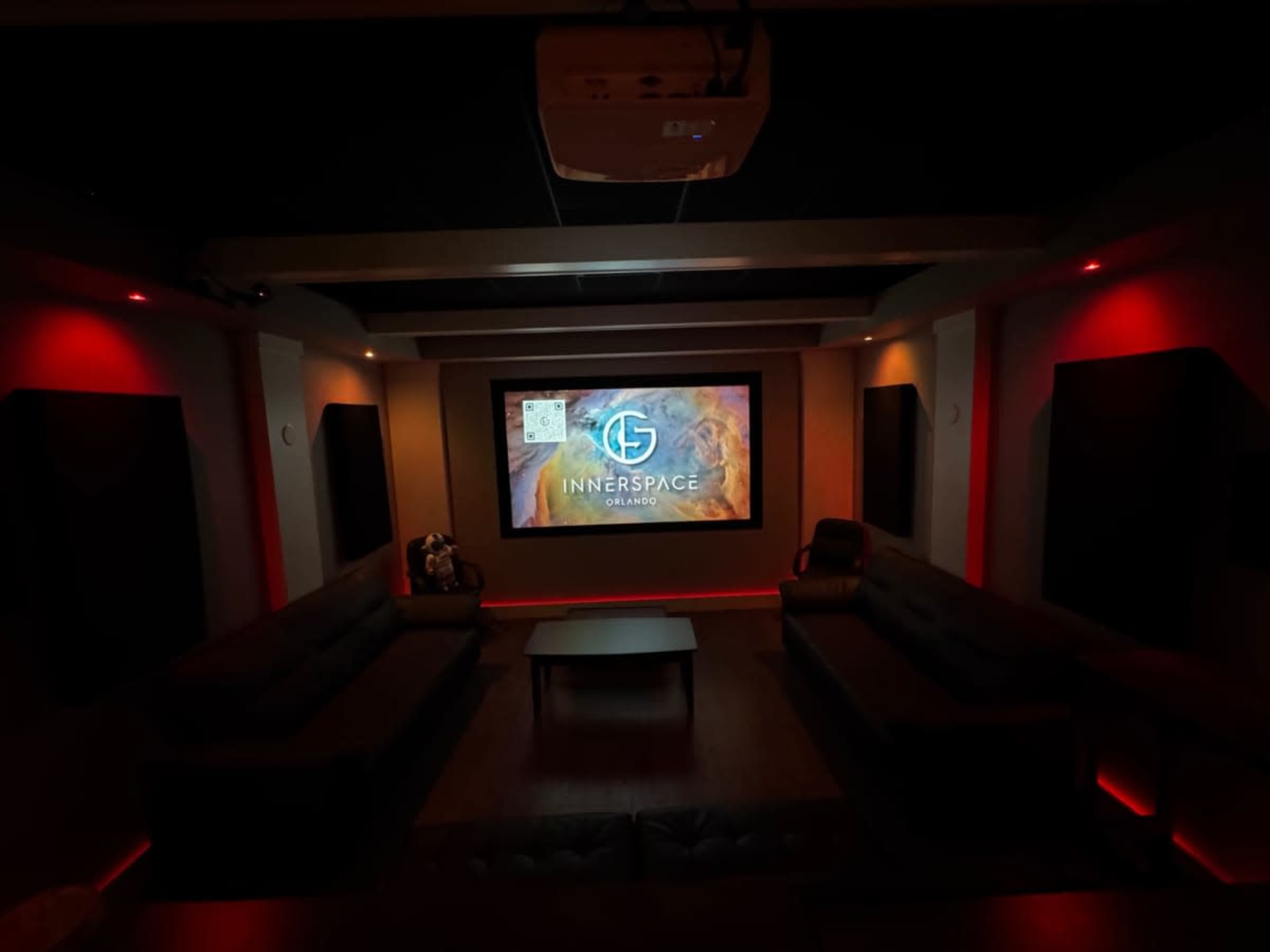The image shows a home theater with a large projection screen displaying the "InnerSpace" logo, surrounded by dark seating and red accent lighting.