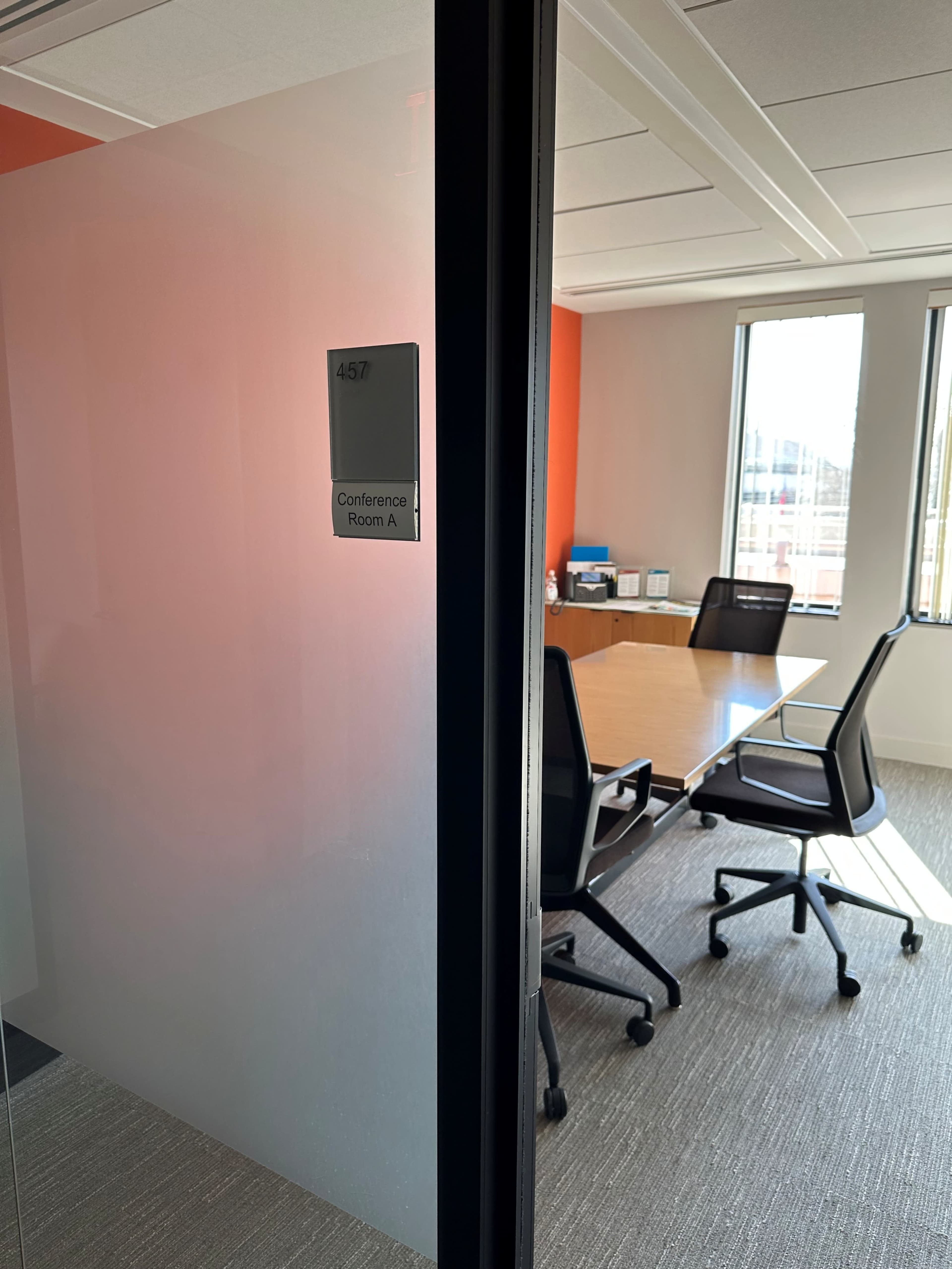 The image shows a partially opened glass door labeled "Conference Room A" leading into a meeting room with a large table and several chairs.