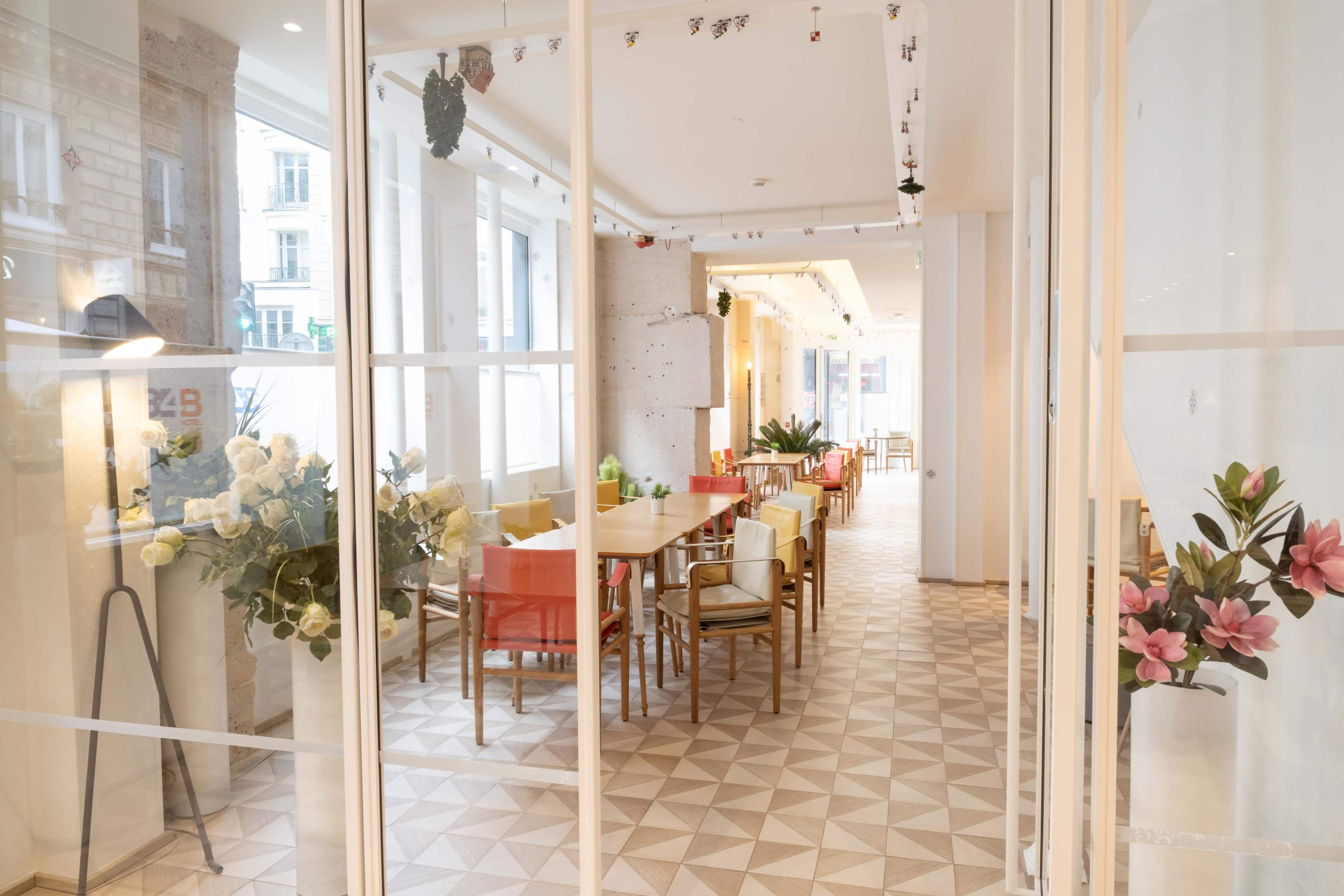 The image shows a modern interior space with a dining area featuring wooden tables, colorful chairs, and decorative plants.