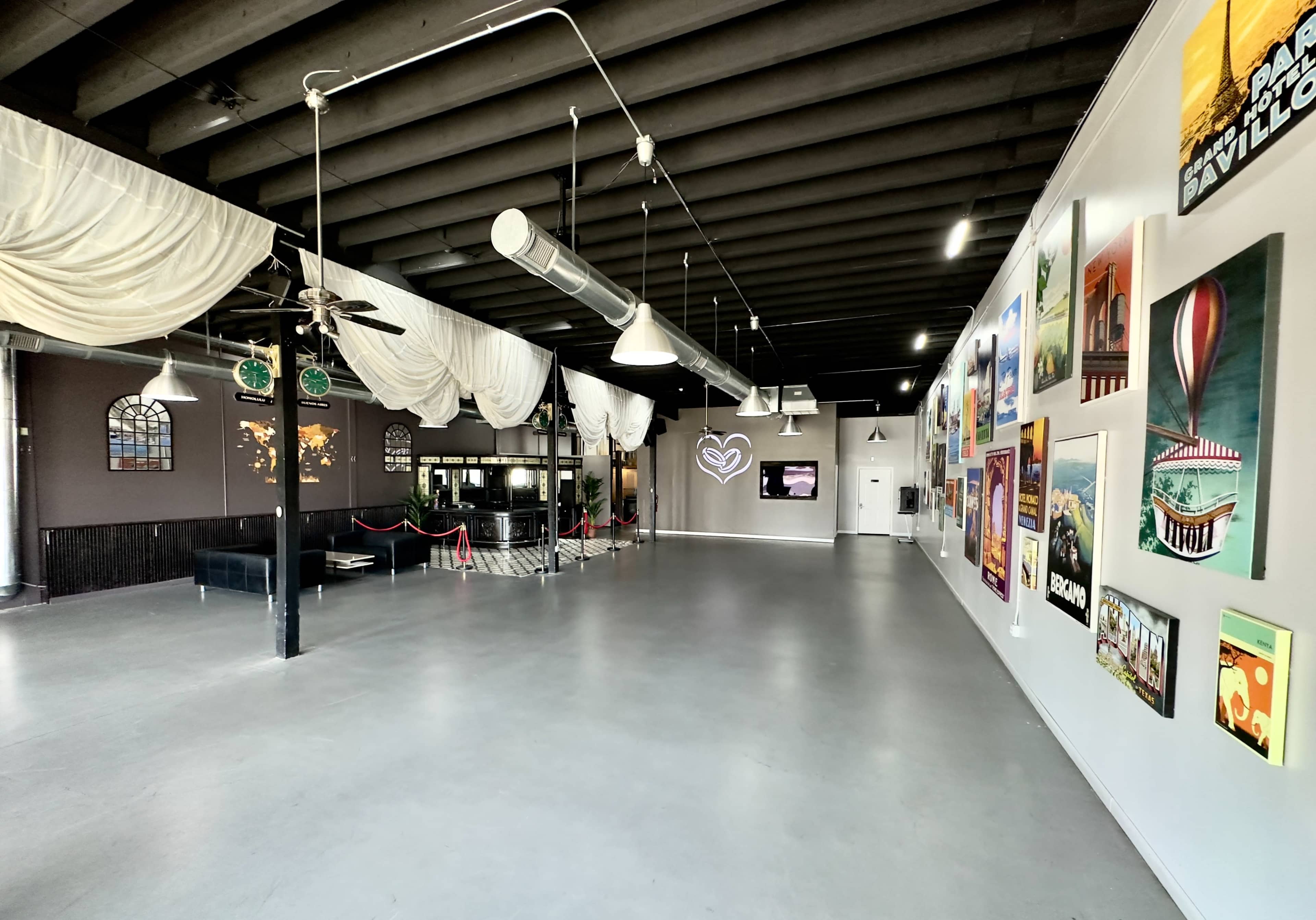 A spacious indoor venue with large windows, hanging drapes, and various art pieces displayed on the walls.