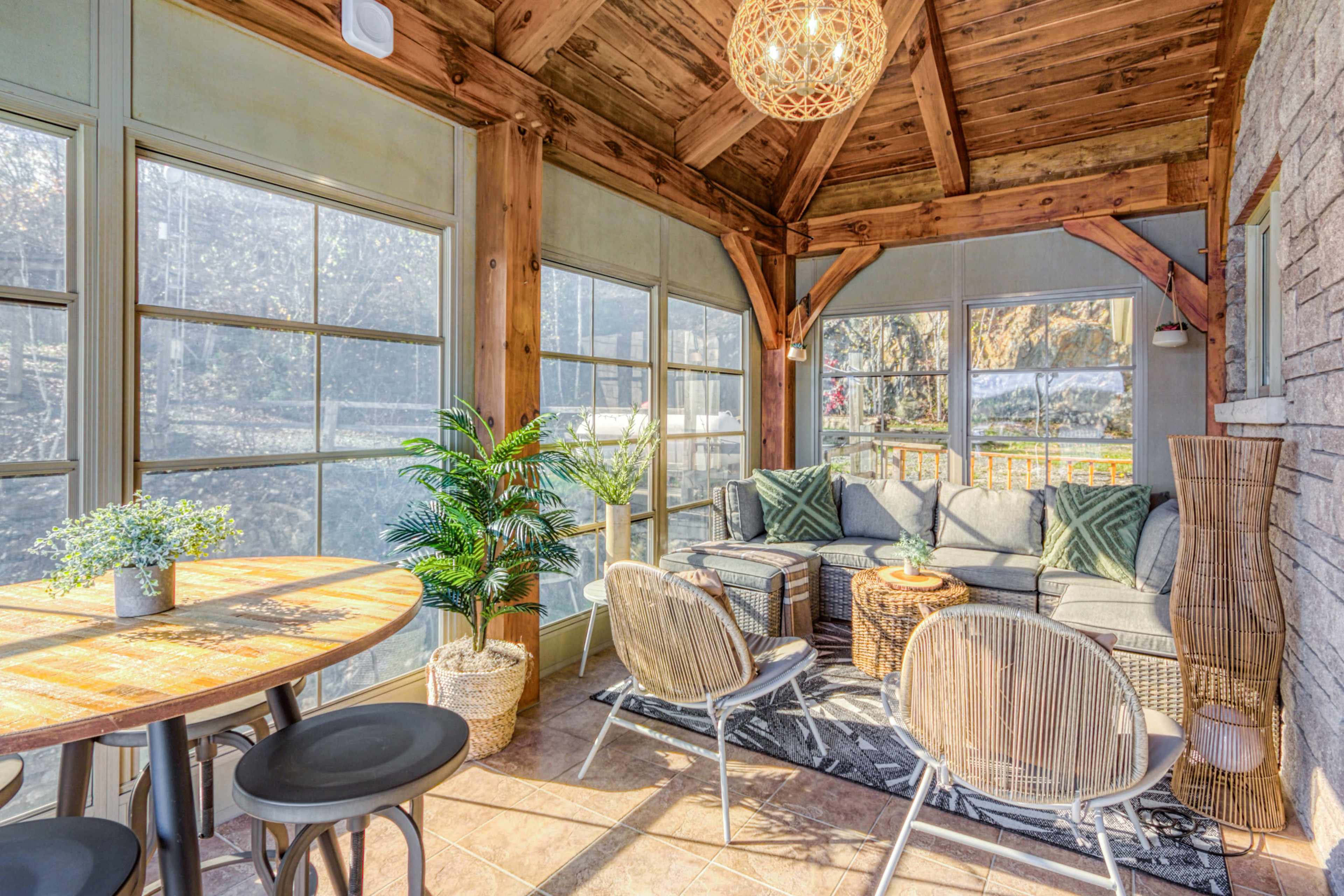 A sunlit sunroom features a cozy seating area with a sectional sofa, surrounded by large windows and potted plants.