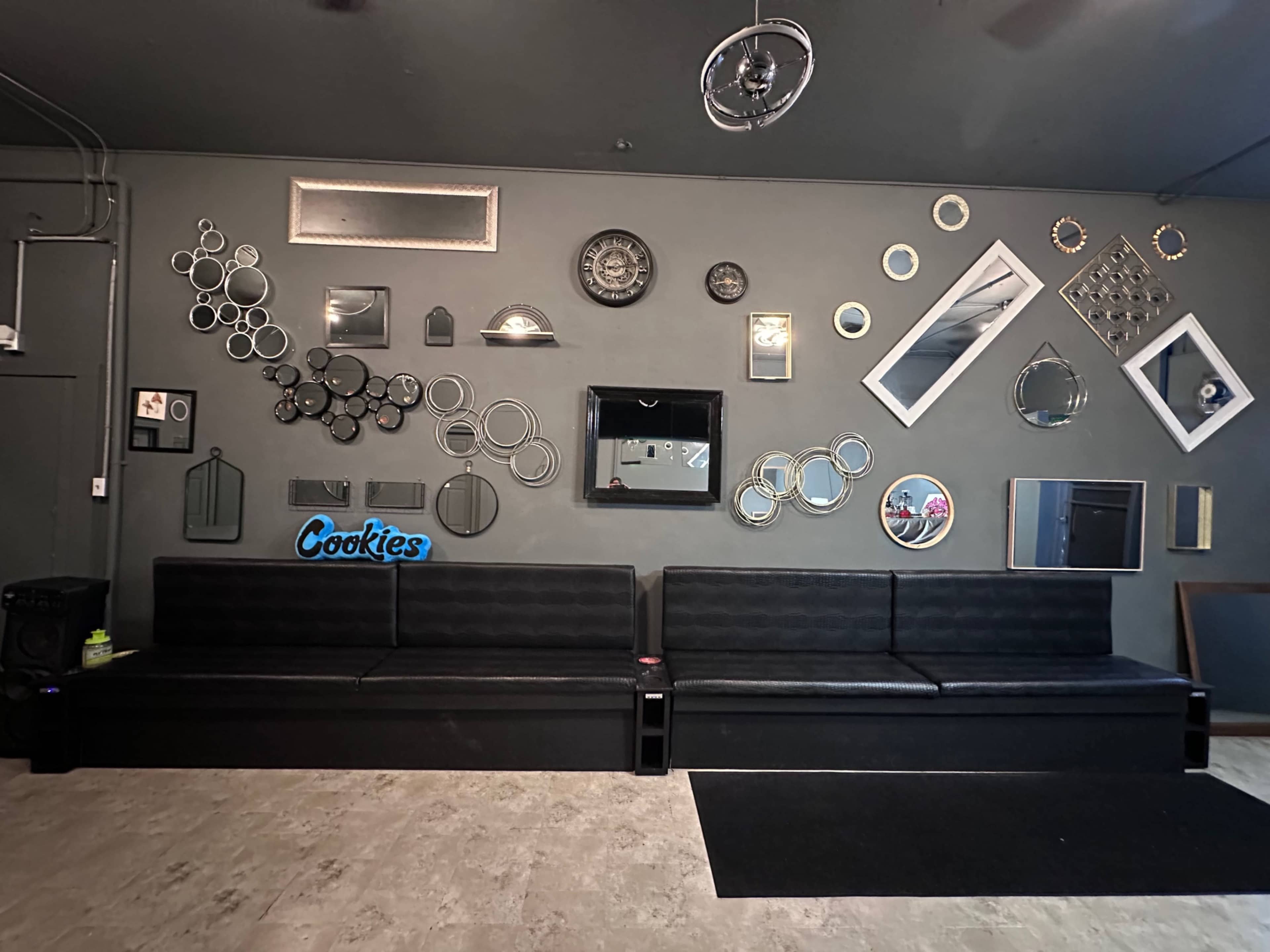 The image shows a wall decorated with various mirrors and wall decor, alongside two black couches and a small black rug in front of them.