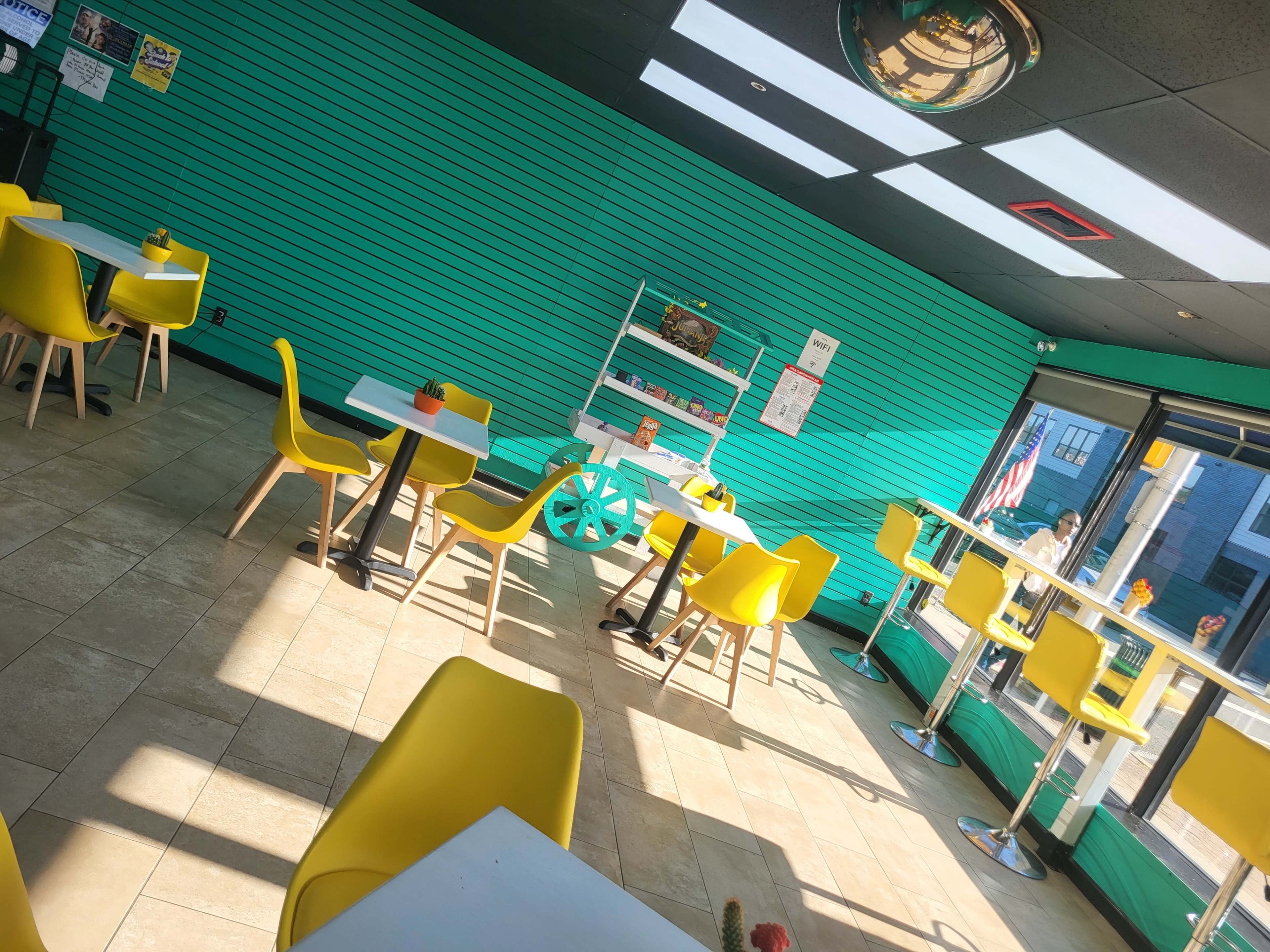 A brightly lit café with turquoise striped walls and yellow chairs arranged around white tables.