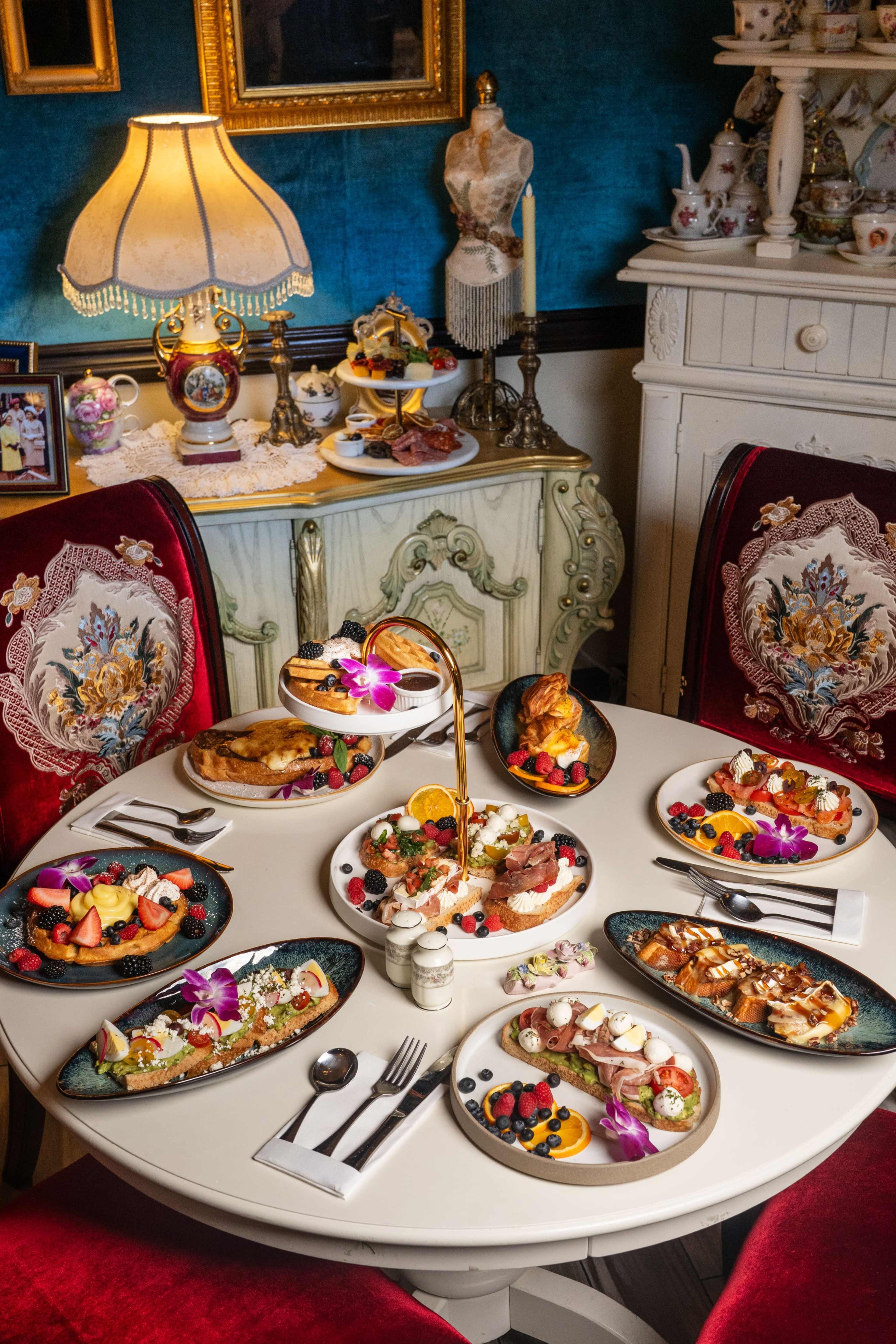 A lavishly set table displays an array of beautifully plated dishes, including fruits, pastries, and desserts, surrounded by elegant decor in a cozy dining room.