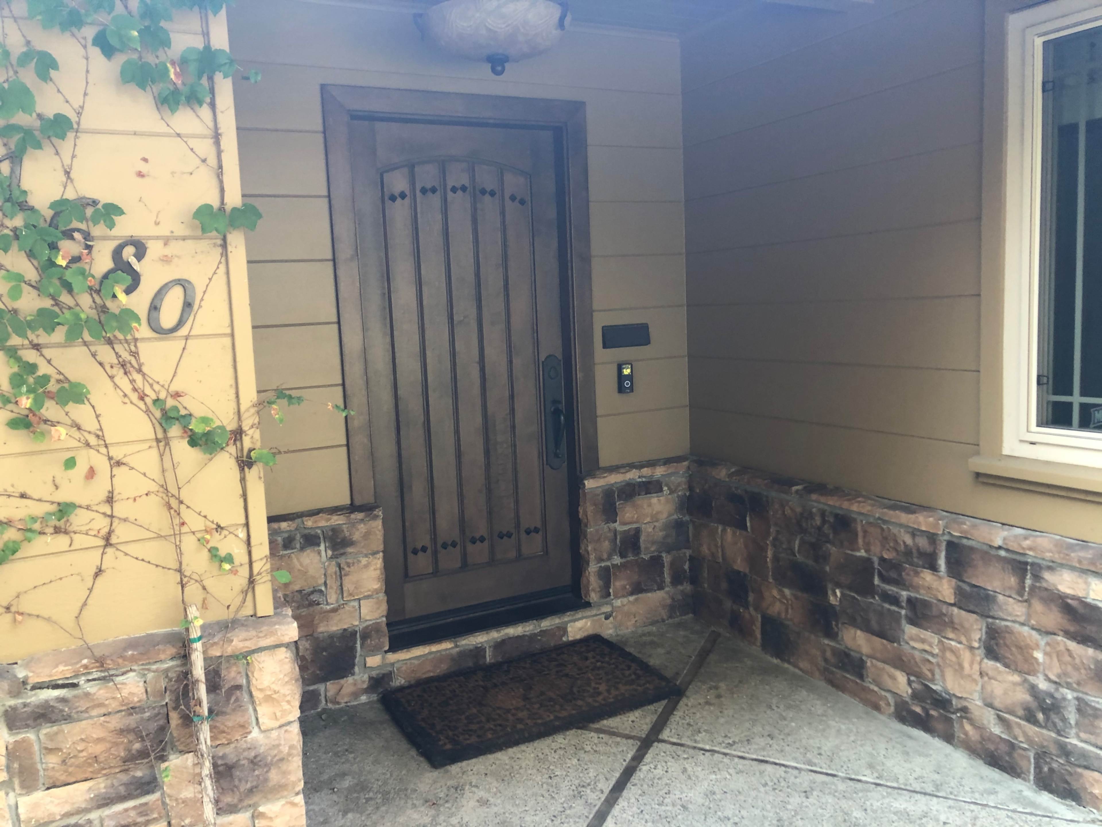 An entrance with a wooden door featuring decorative accents, surrounded by stone wall cladding and a welcome mat on the concrete floor.