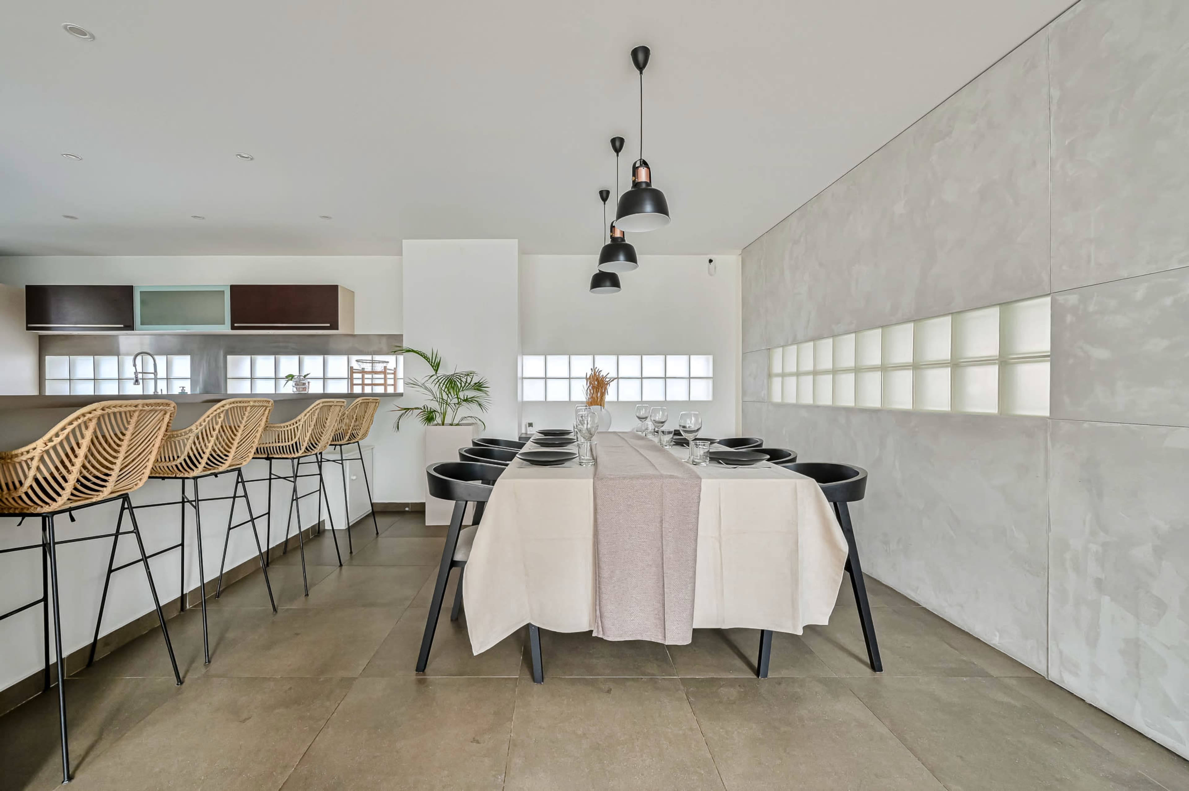 A modern dining area features a table set for a meal, with black chairs and pendant lighting overhead.
