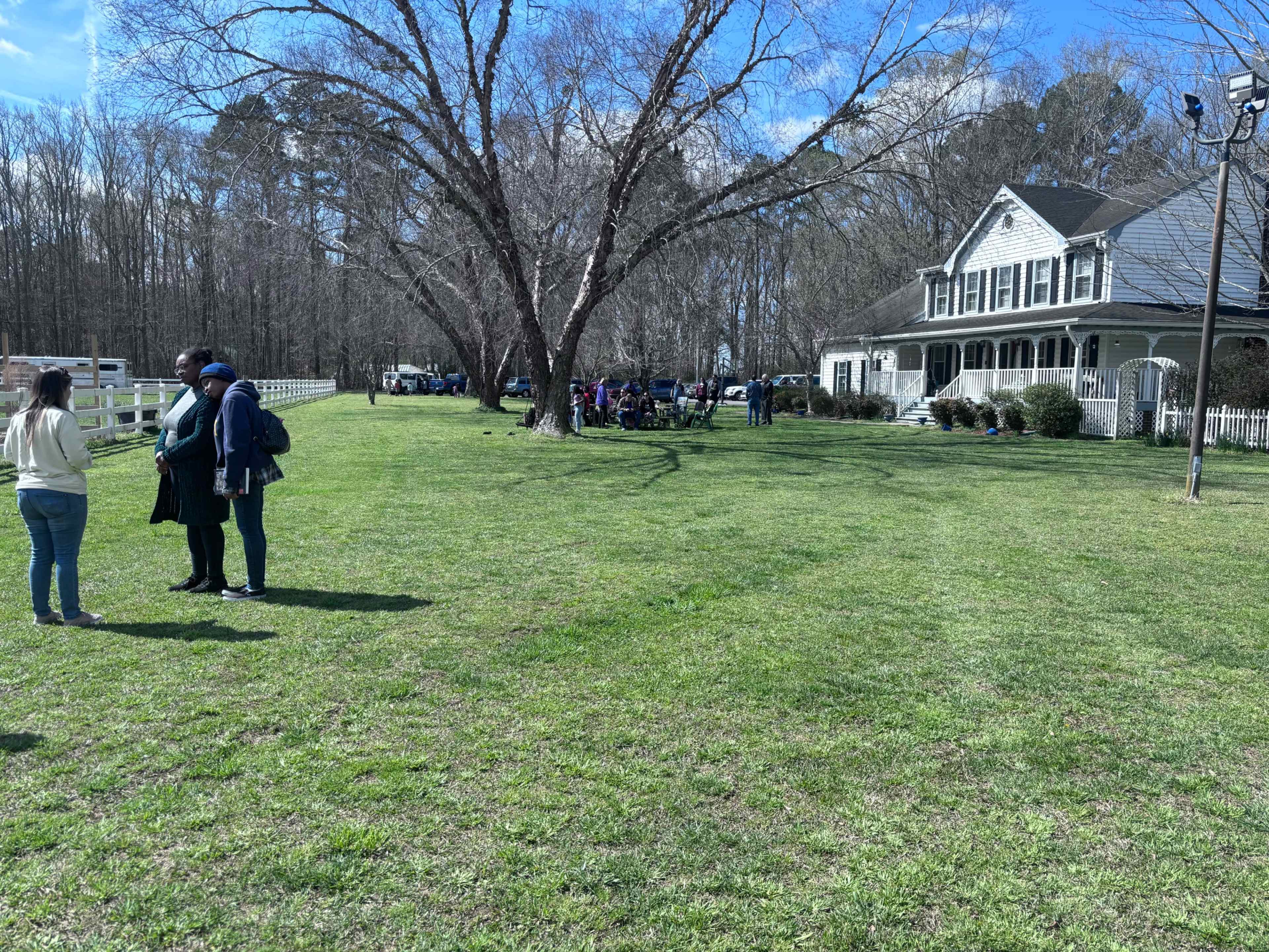 A large yard with a tree and a house in the background, where several people are gathered for an outdoor event.