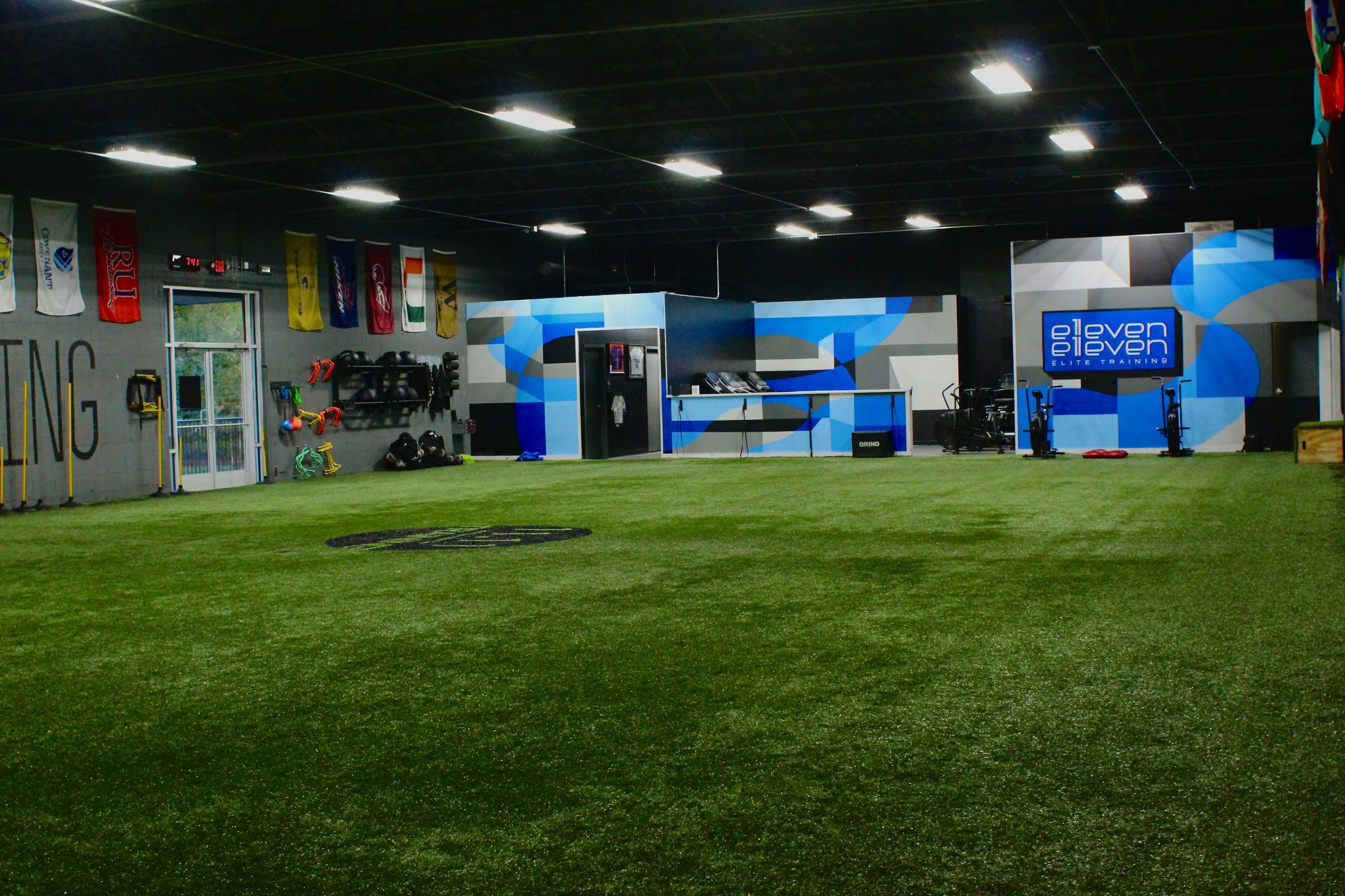 A spacious indoor training facility with artificial turf, exercise equipment, and colorful wall graphics.