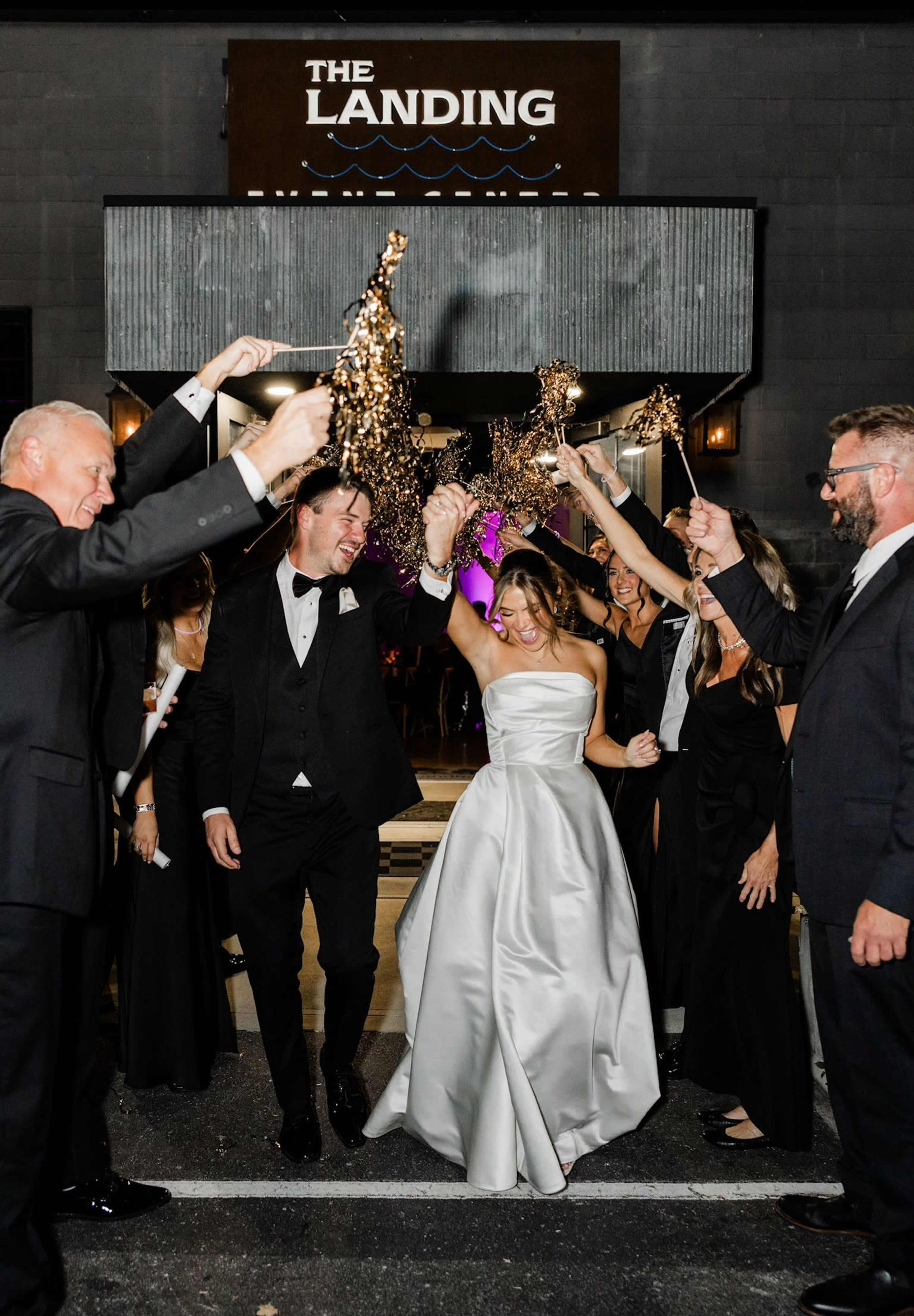 A newlywed couple exits a venue called "The Landing" while guests celebrate with sparklers.