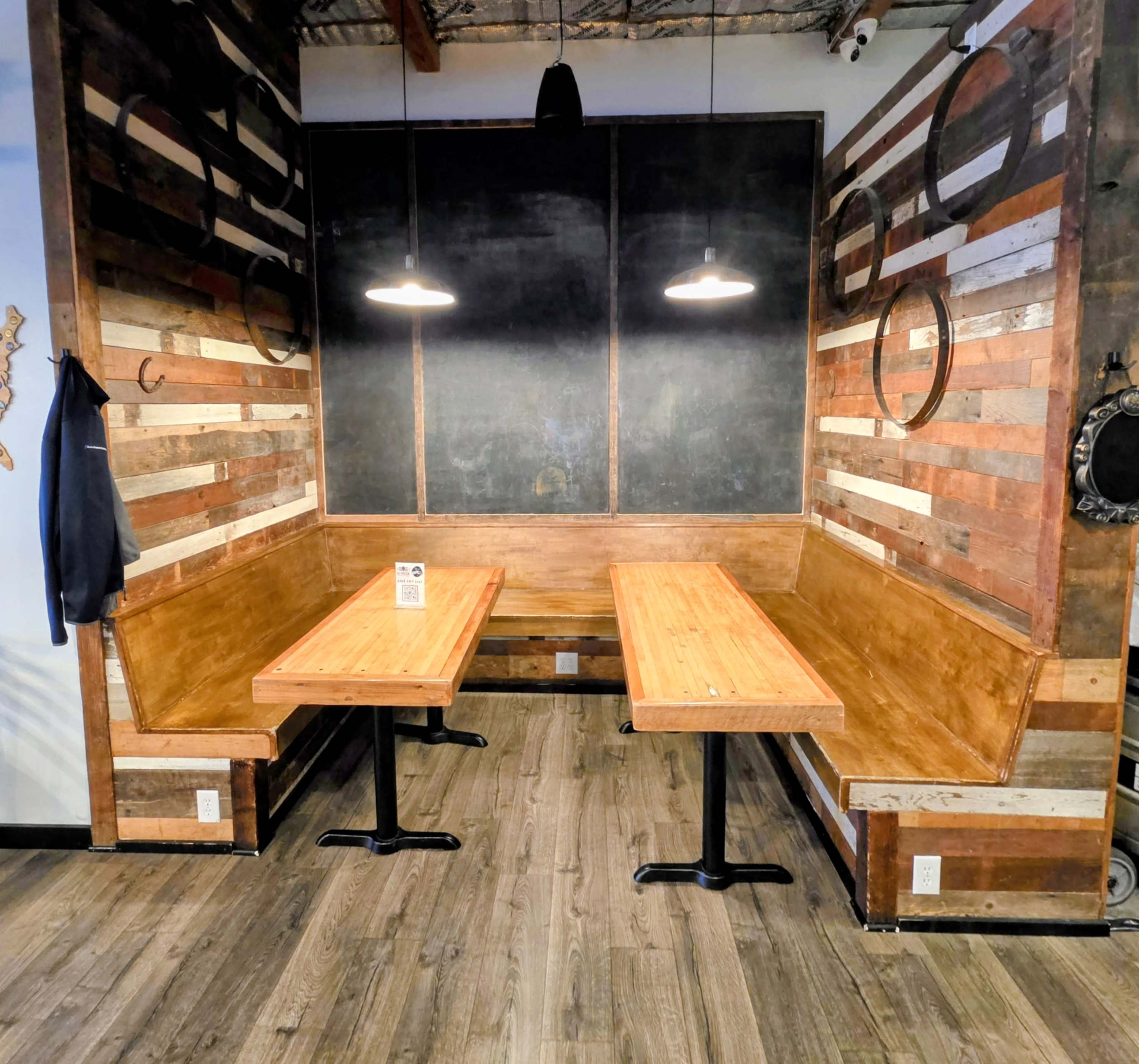 The image shows a wooden corner booth with two long tables and pendant lights in a restaurant setting.