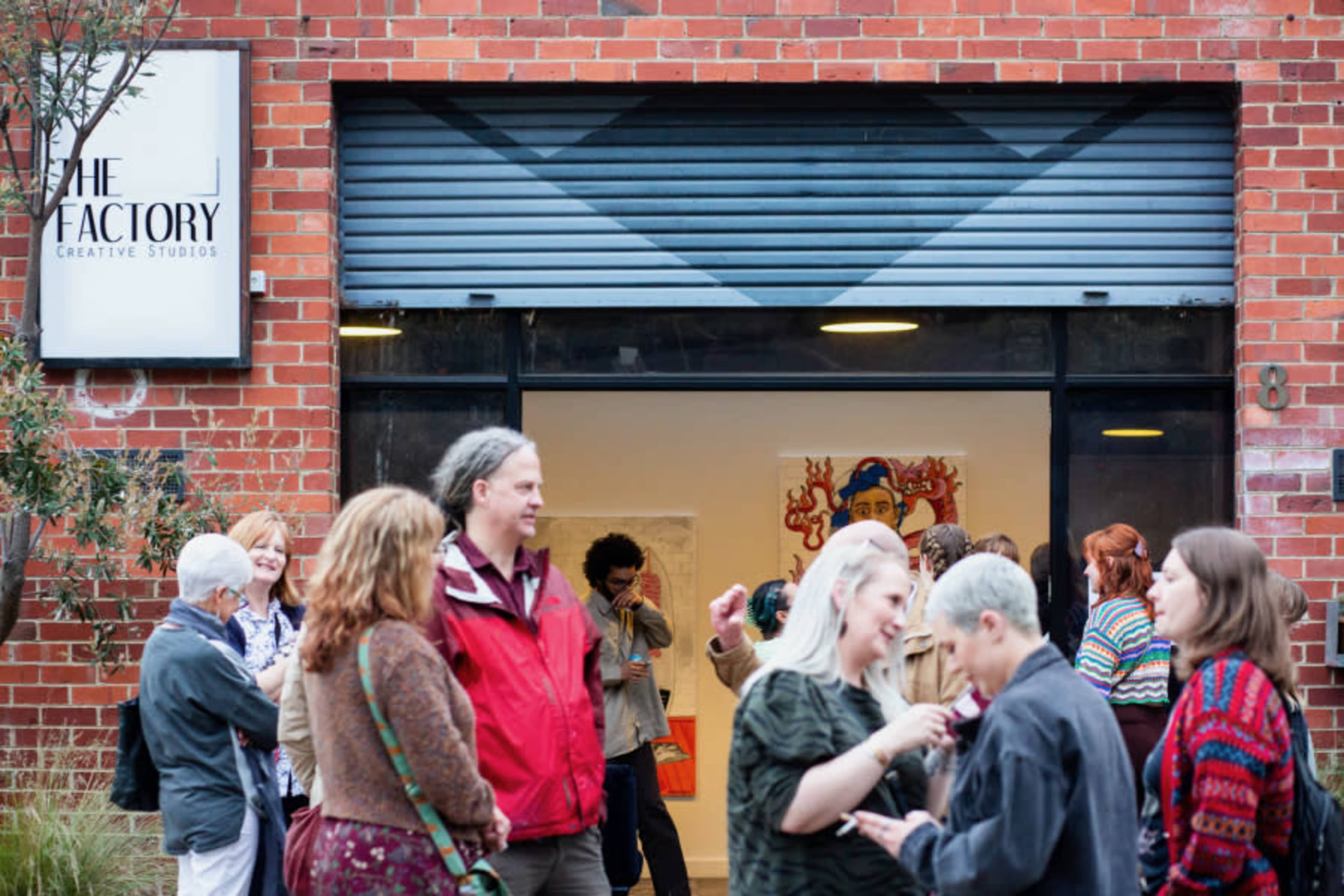 A group of people gathers outside a building with a sign reading "THE FACTORY Creative Studios."
