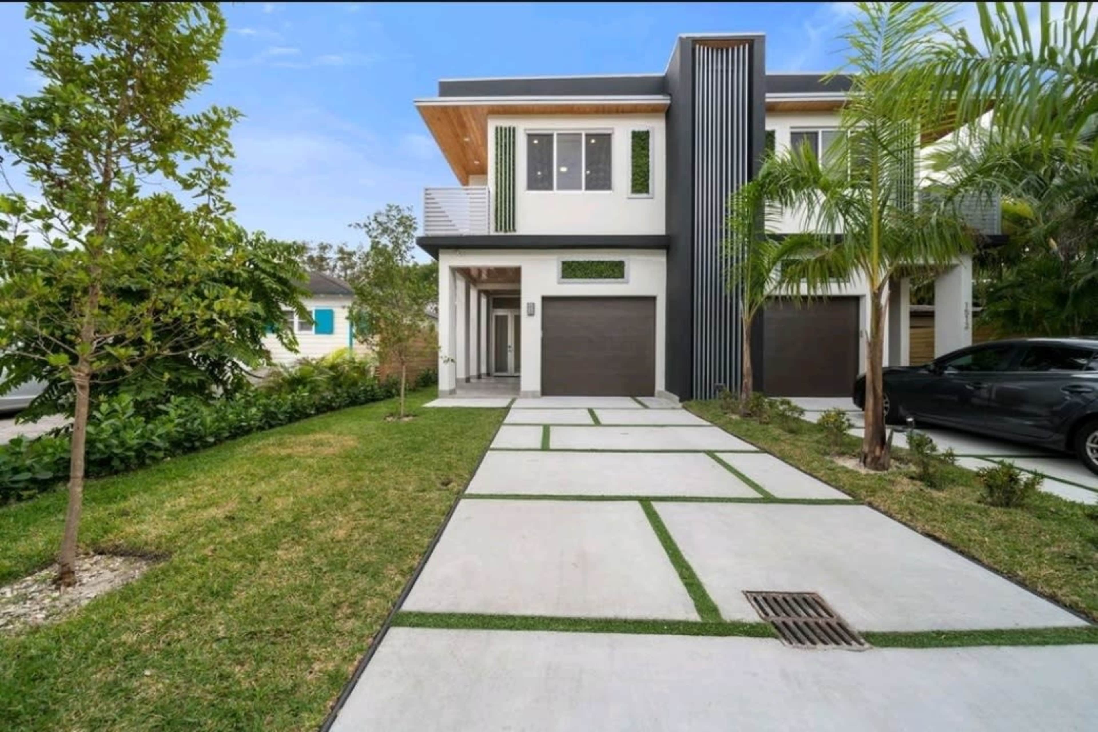 The image shows a modern two-story house with a landscaped front yard, featuring a concrete driveway and green accents.