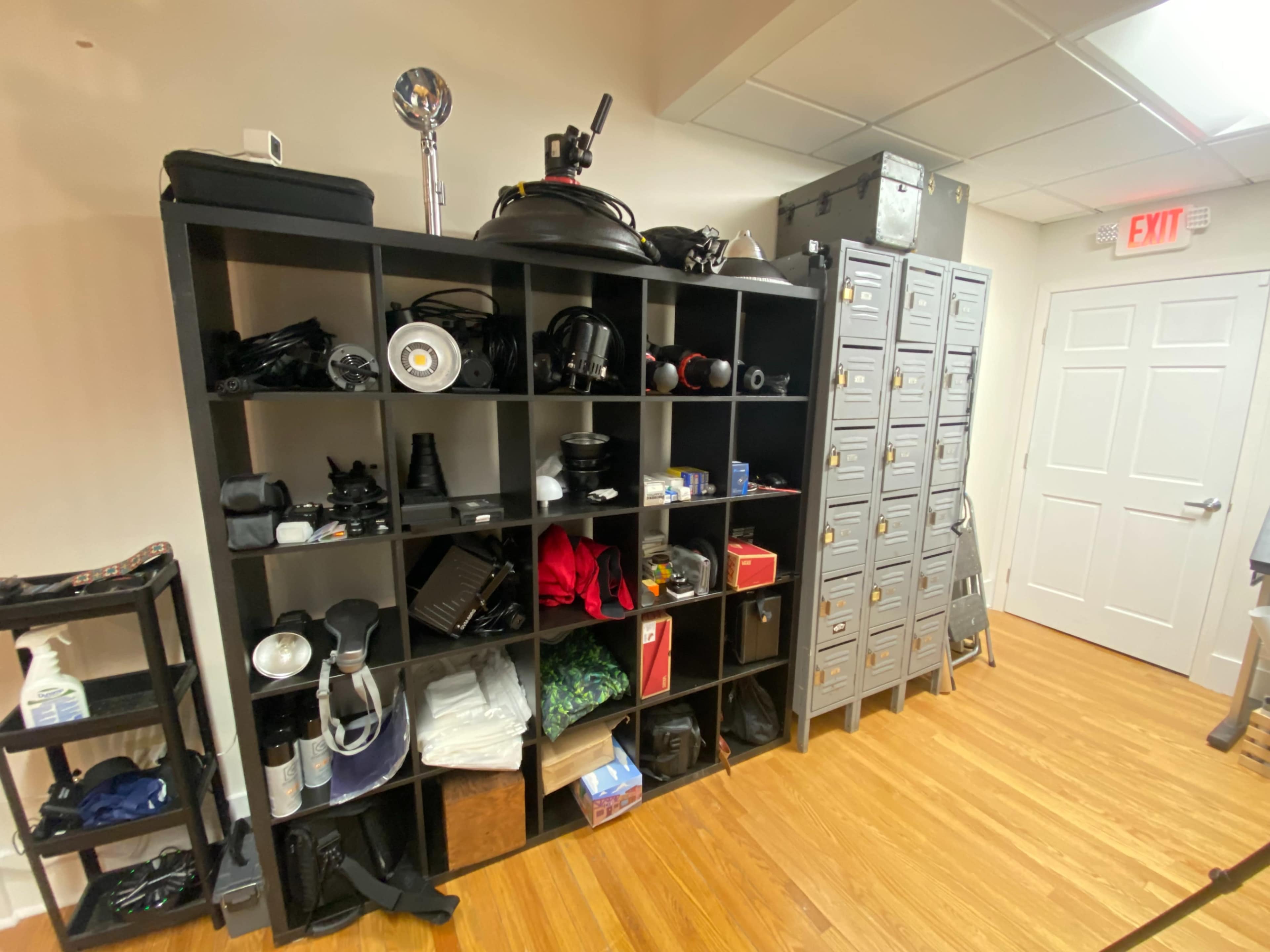 A shelving unit filled with various tools and equipment is displayed against a light-colored wall, next to a door with a clear exit sign.