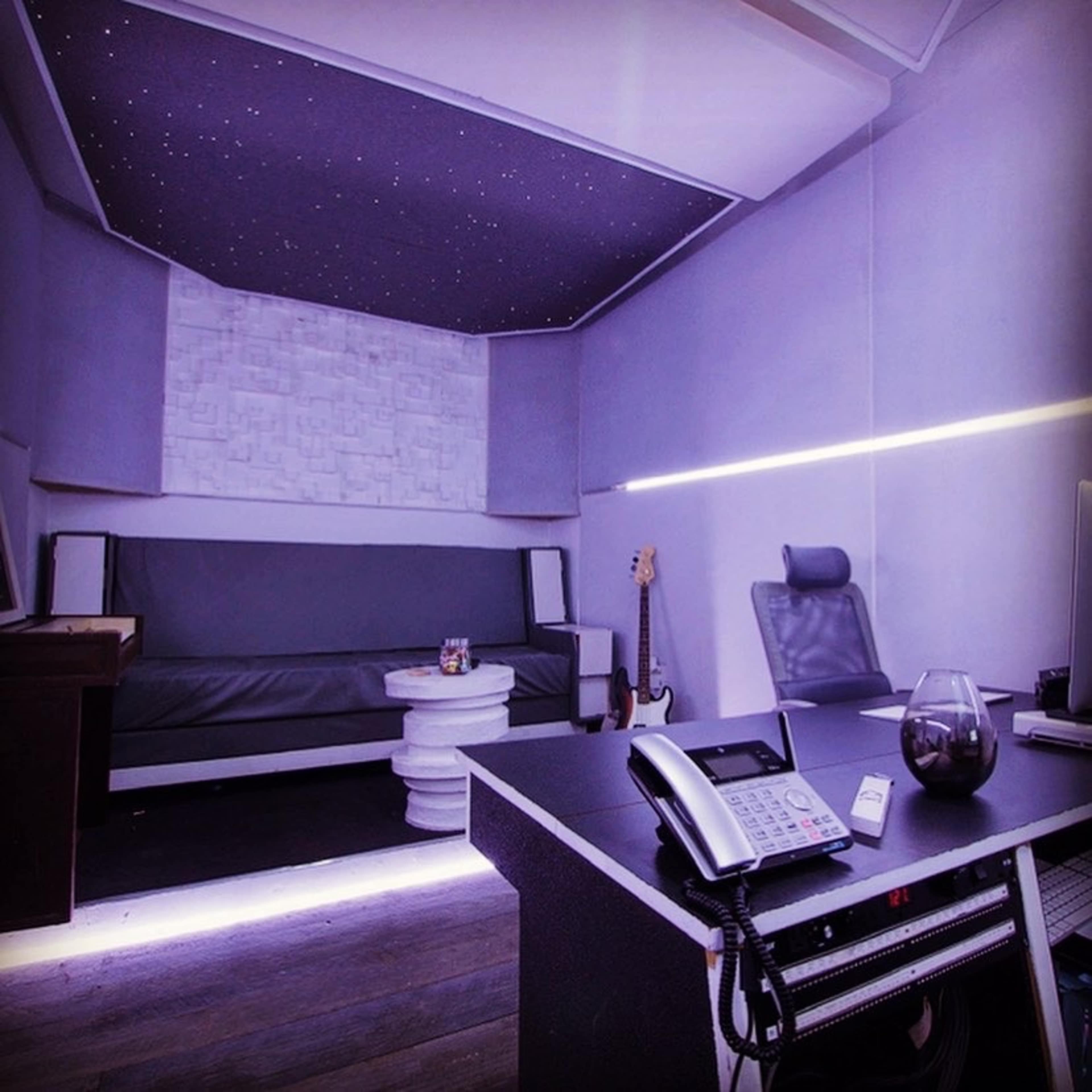 A modern office space featuring a couch, a desk with a phone, and ambient lighting on the walls and ceiling.