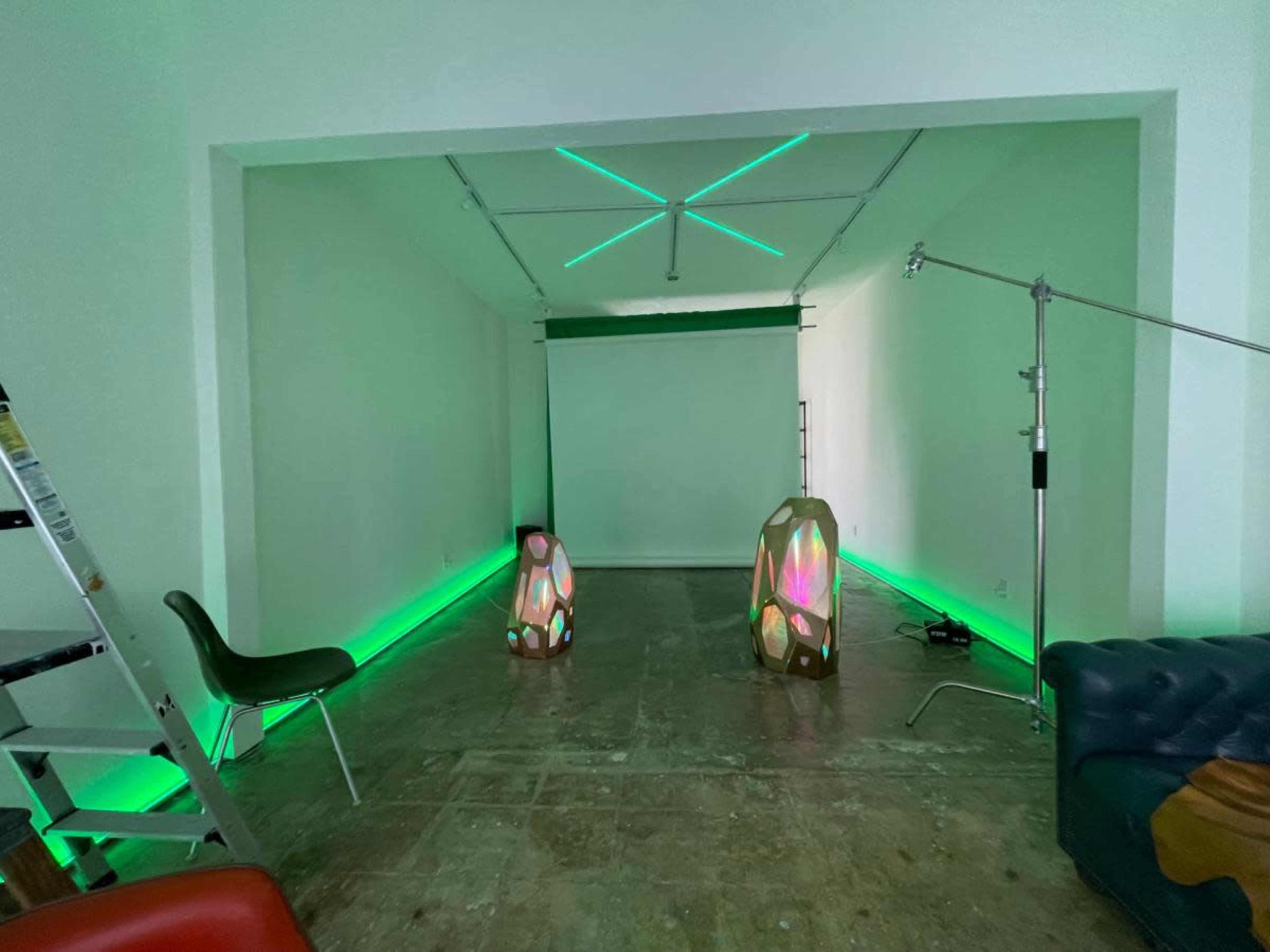 The image shows a spacious room with green lighting, featuring two illuminated decorative elements and a projector screen mounted on the wall.