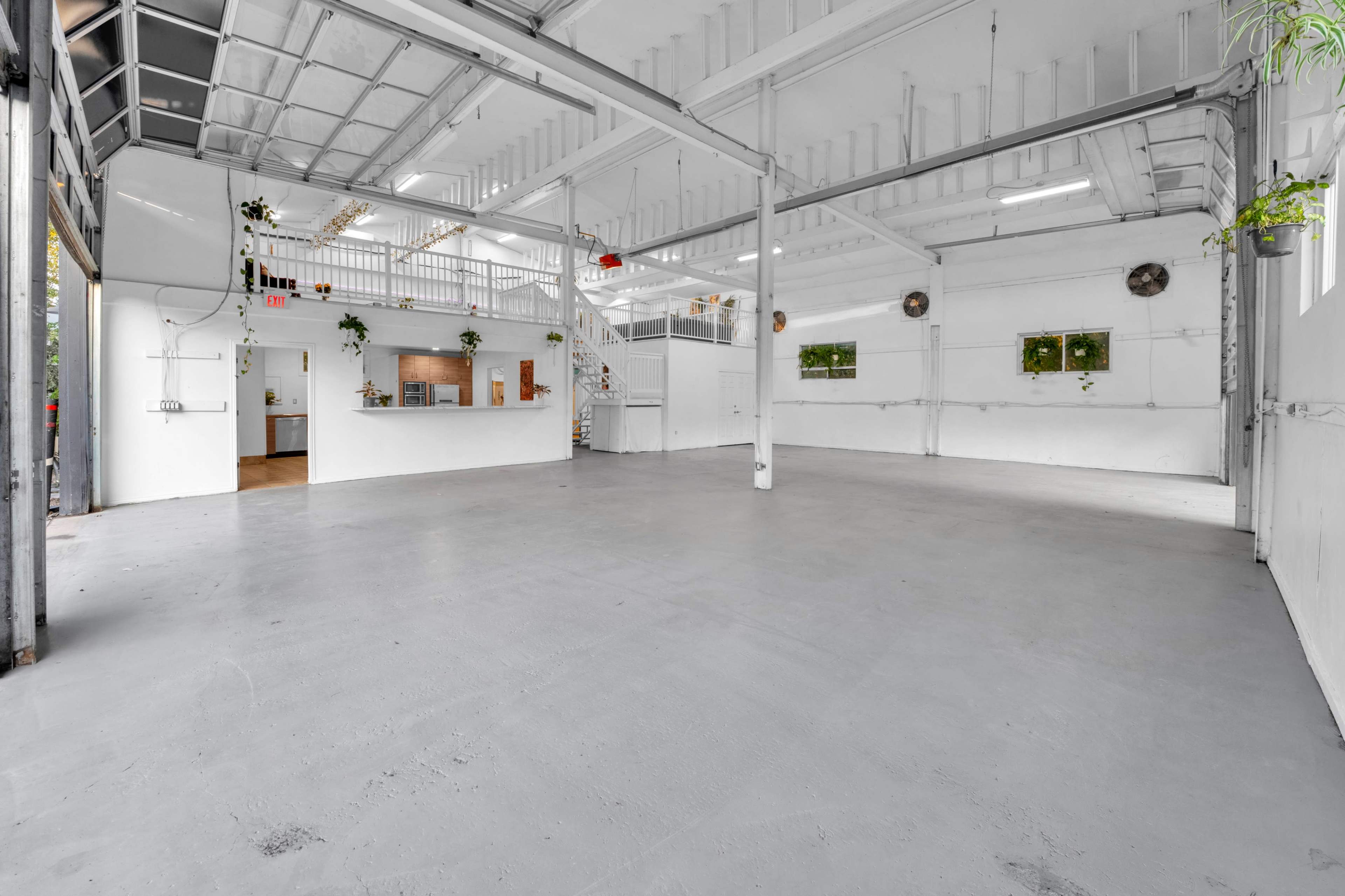 The image shows a spacious, empty interior of a bright, industrial-style room with white walls and a concrete floor.