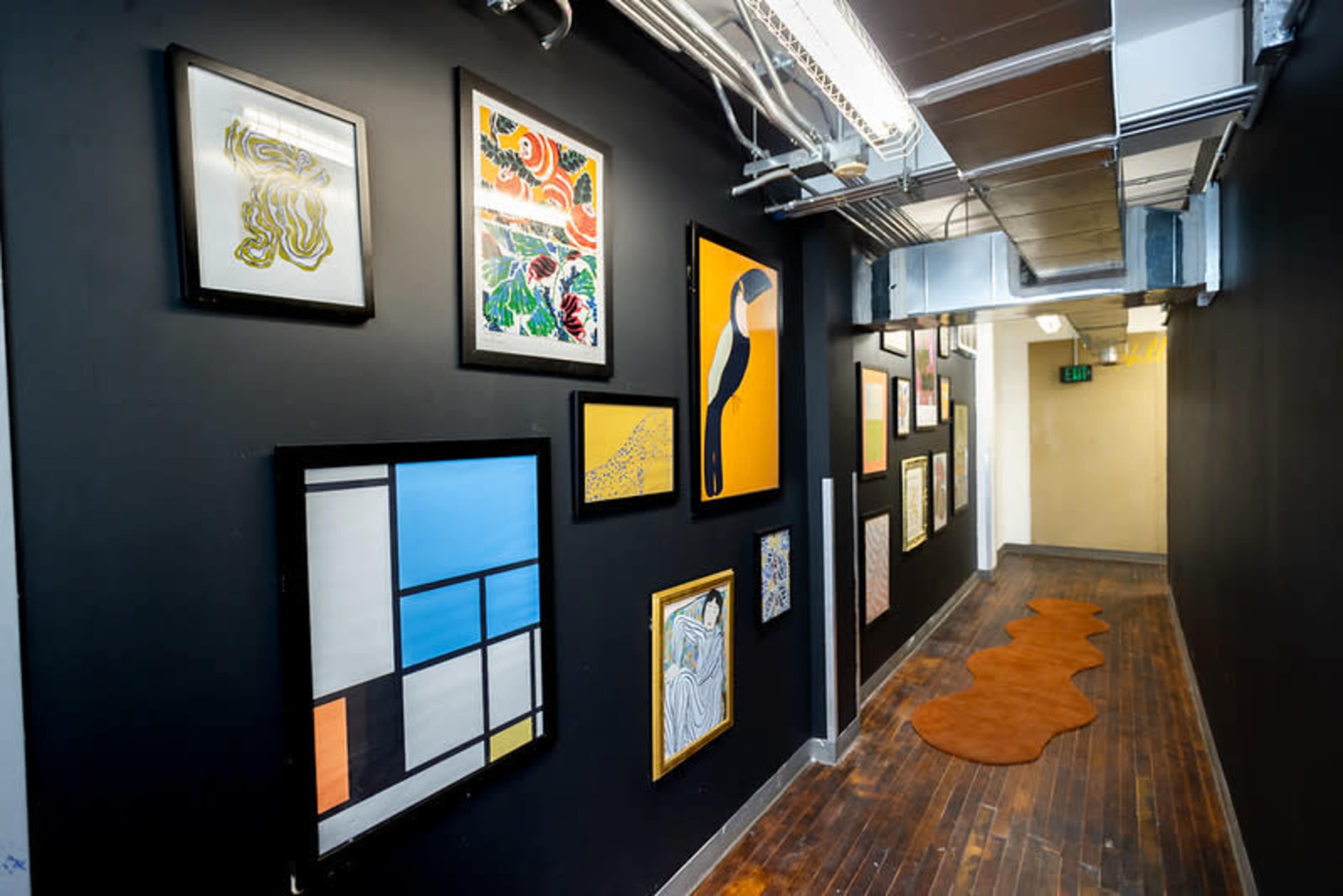 The image shows a narrow hallway with framed artwork on the walls and a patterned rug on the wooden floor.