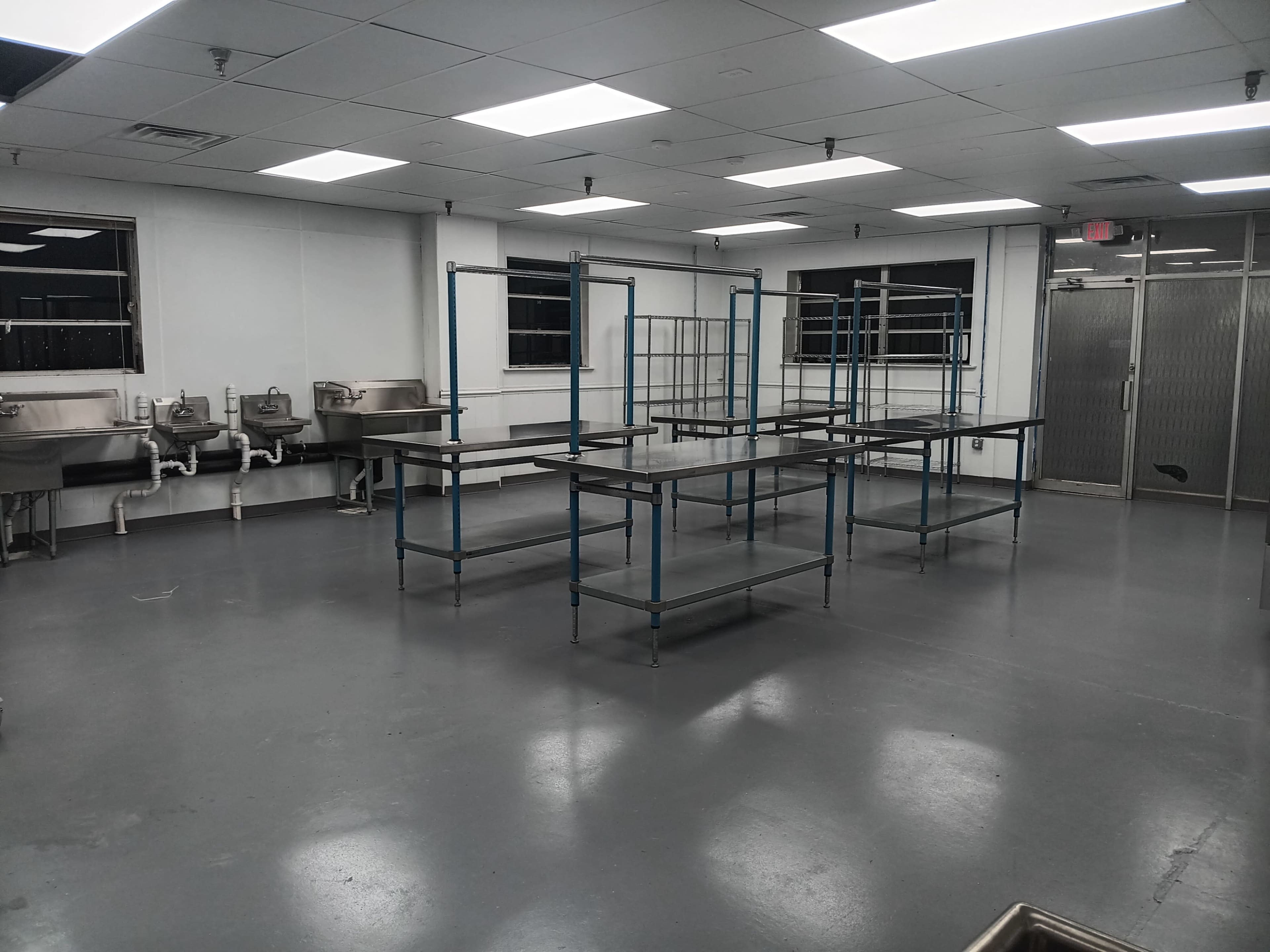 The image shows a spacious, undecorated room with metal shelving units and two stainless steel sinks along the walls.