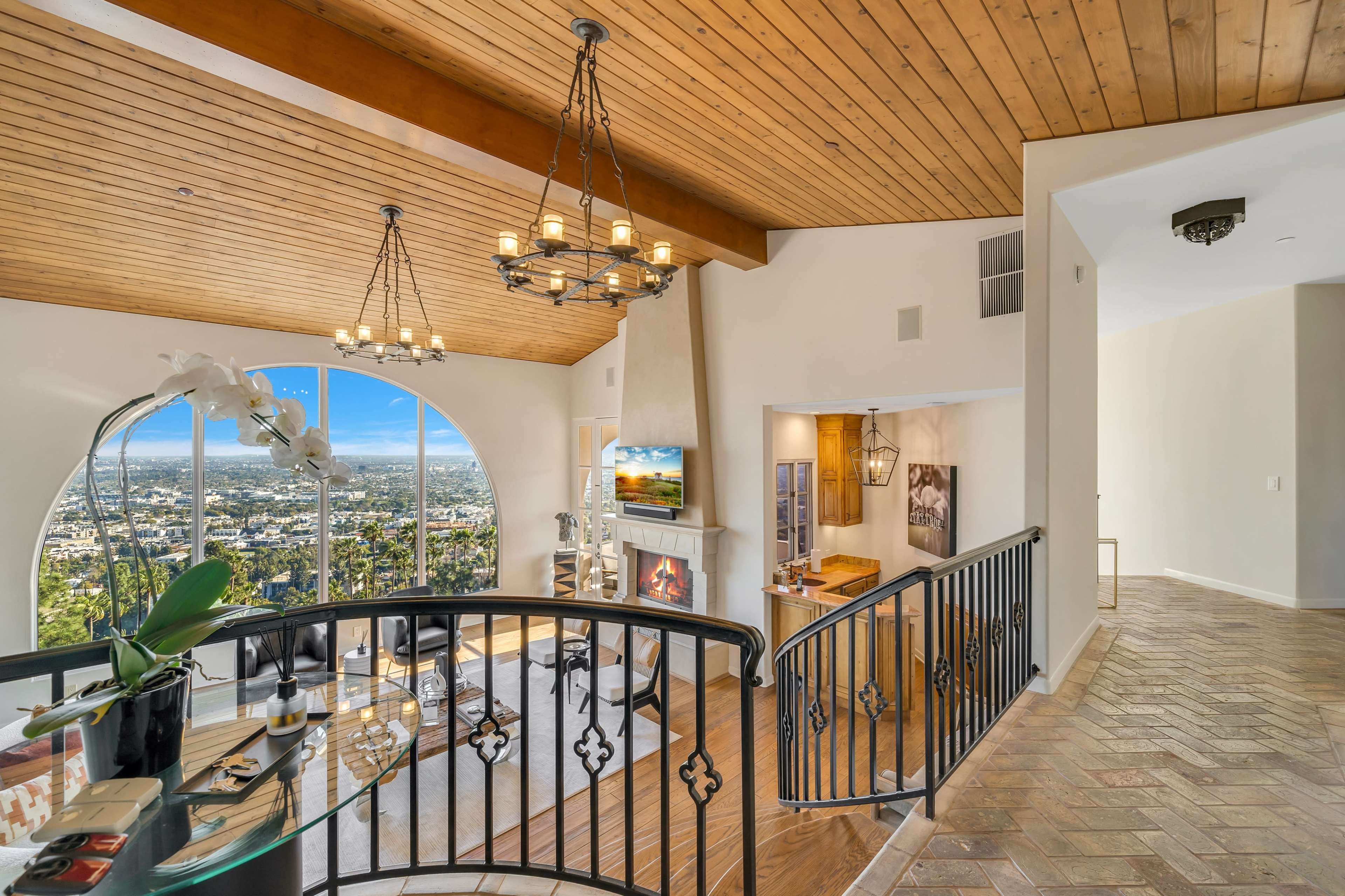 A spacious living room features a vaulted ceiling, large arched windows with city views, and a fireplace near a cozy seating area.