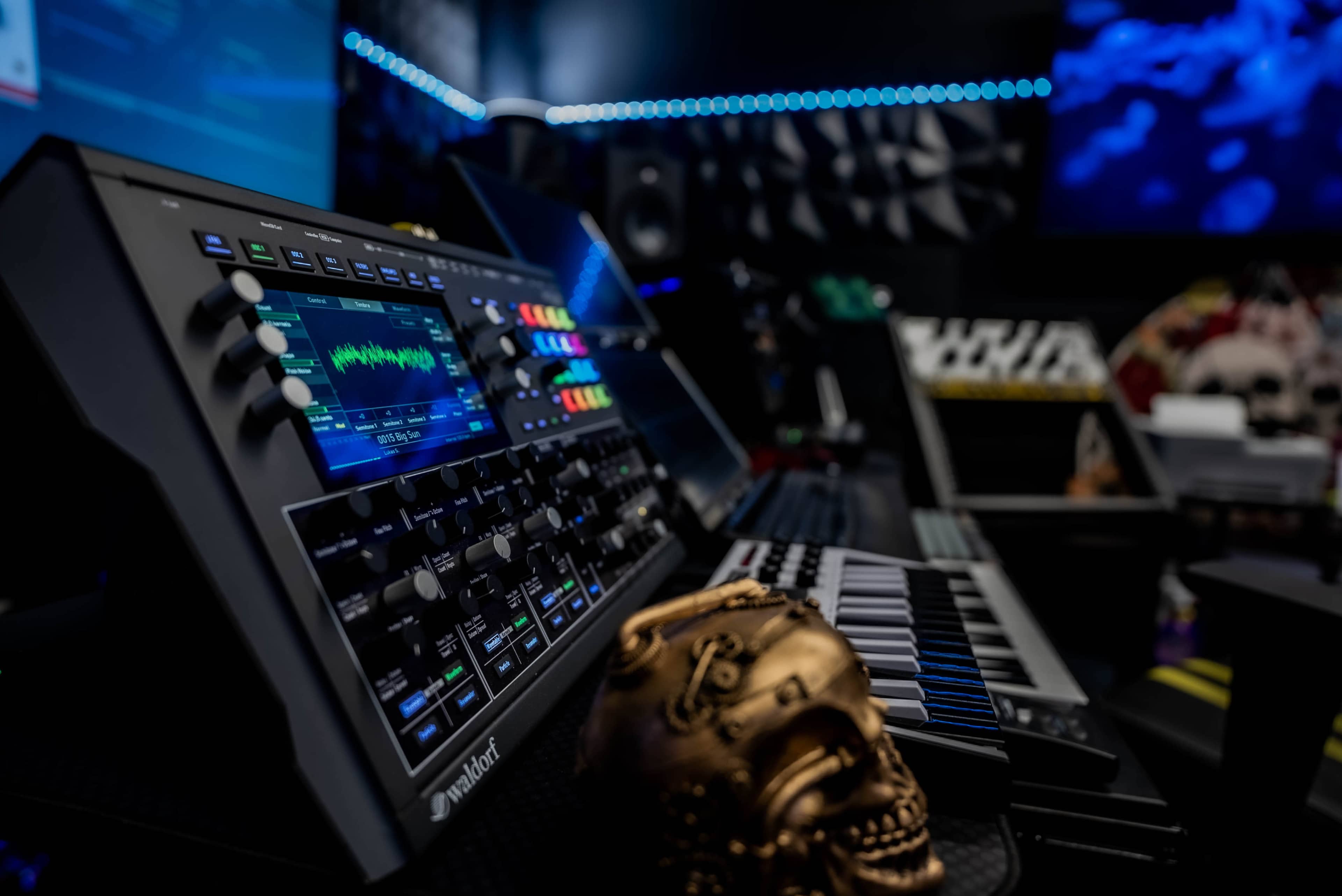 The image shows a close-up of a synthesizer and keyboard setup in a music studio, with a decorative skull in the foreground.