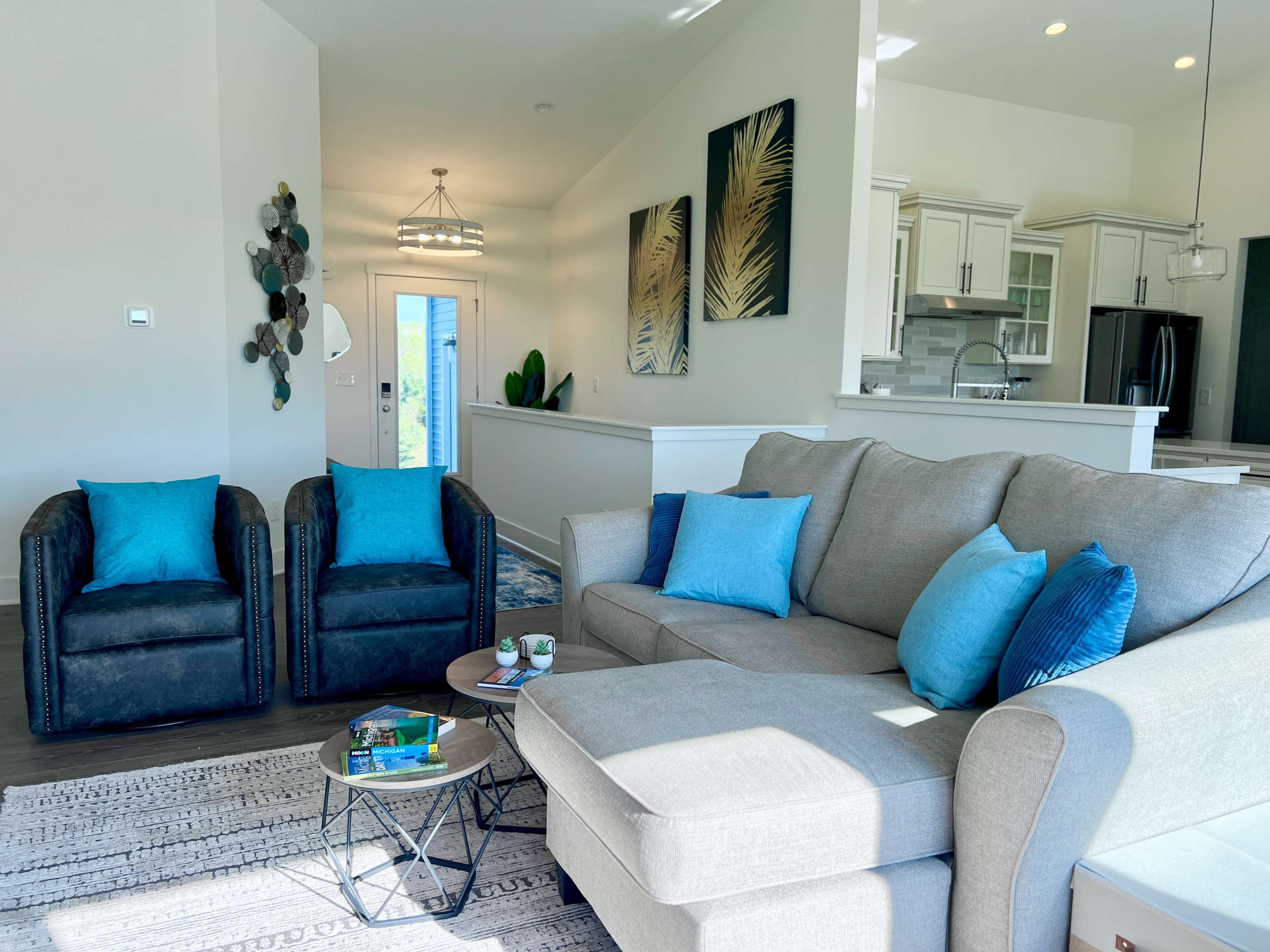 The image shows a modern living room with a gray sofa, two blue-accented chairs, a coffee table, and decorative wall art.