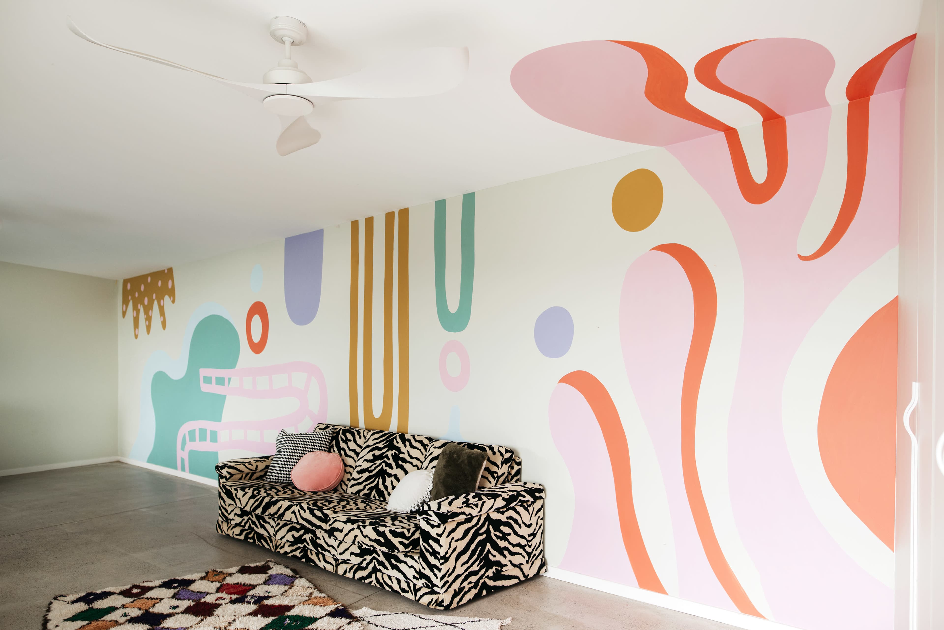 The room features a patterned zebra-print couch against a wall adorned with colorful abstract shapes and designs.