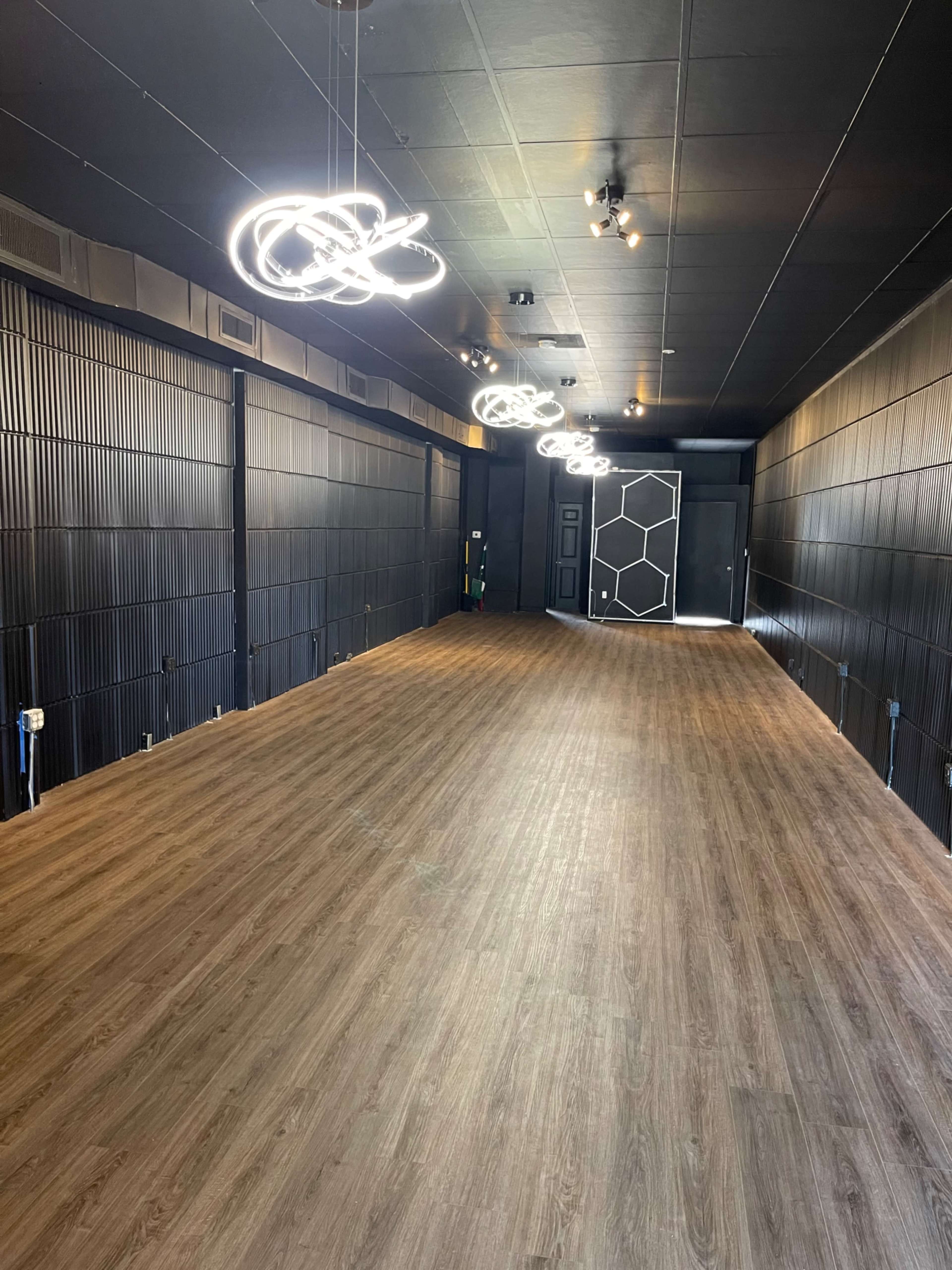 An empty, modern interior space with wooden flooring and illuminated circular light fixtures hanging from the ceiling.
