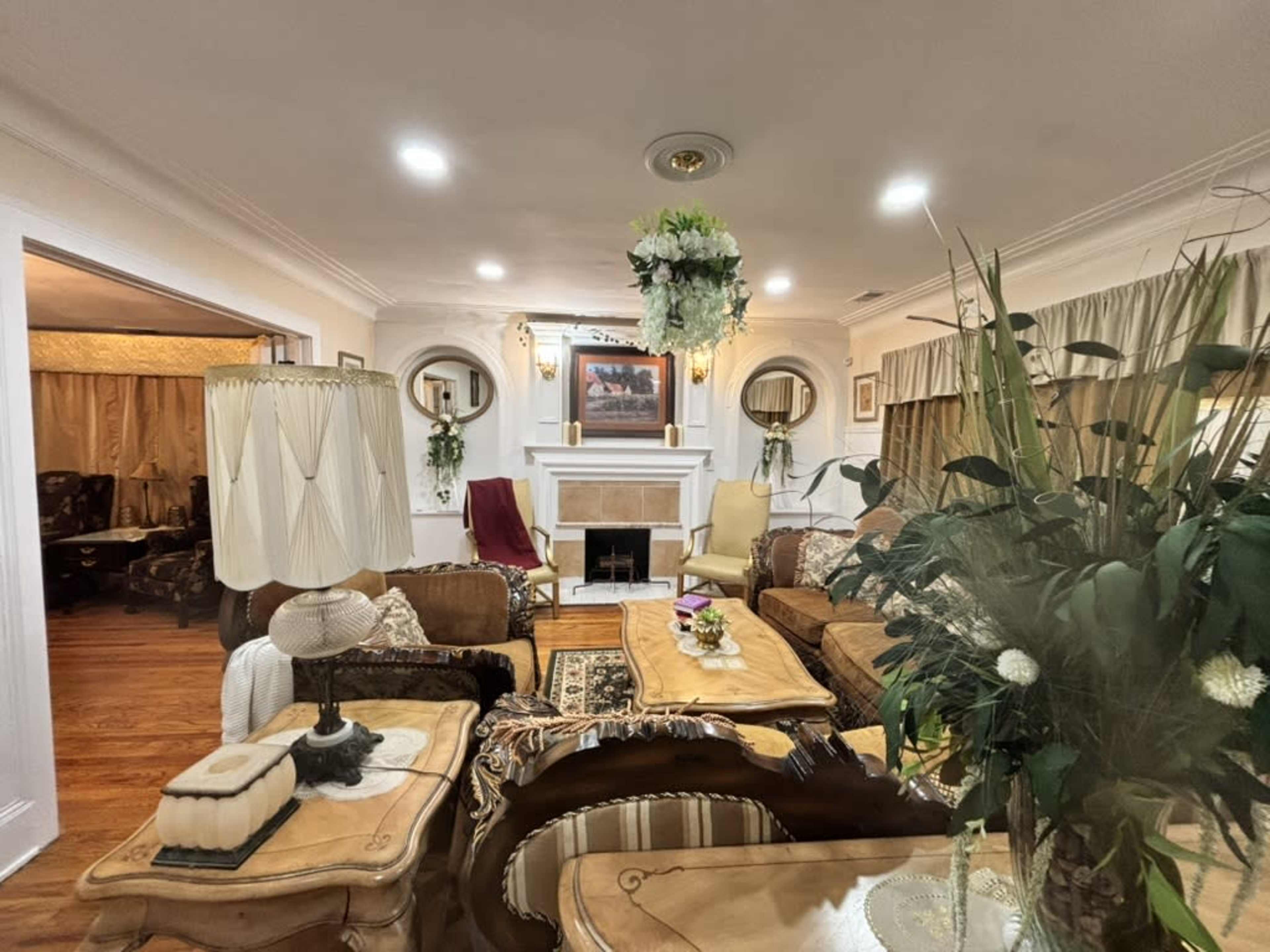 The living room features a fireplace surrounded by seating, decorative plants, and a lighting fixture with floral accents.