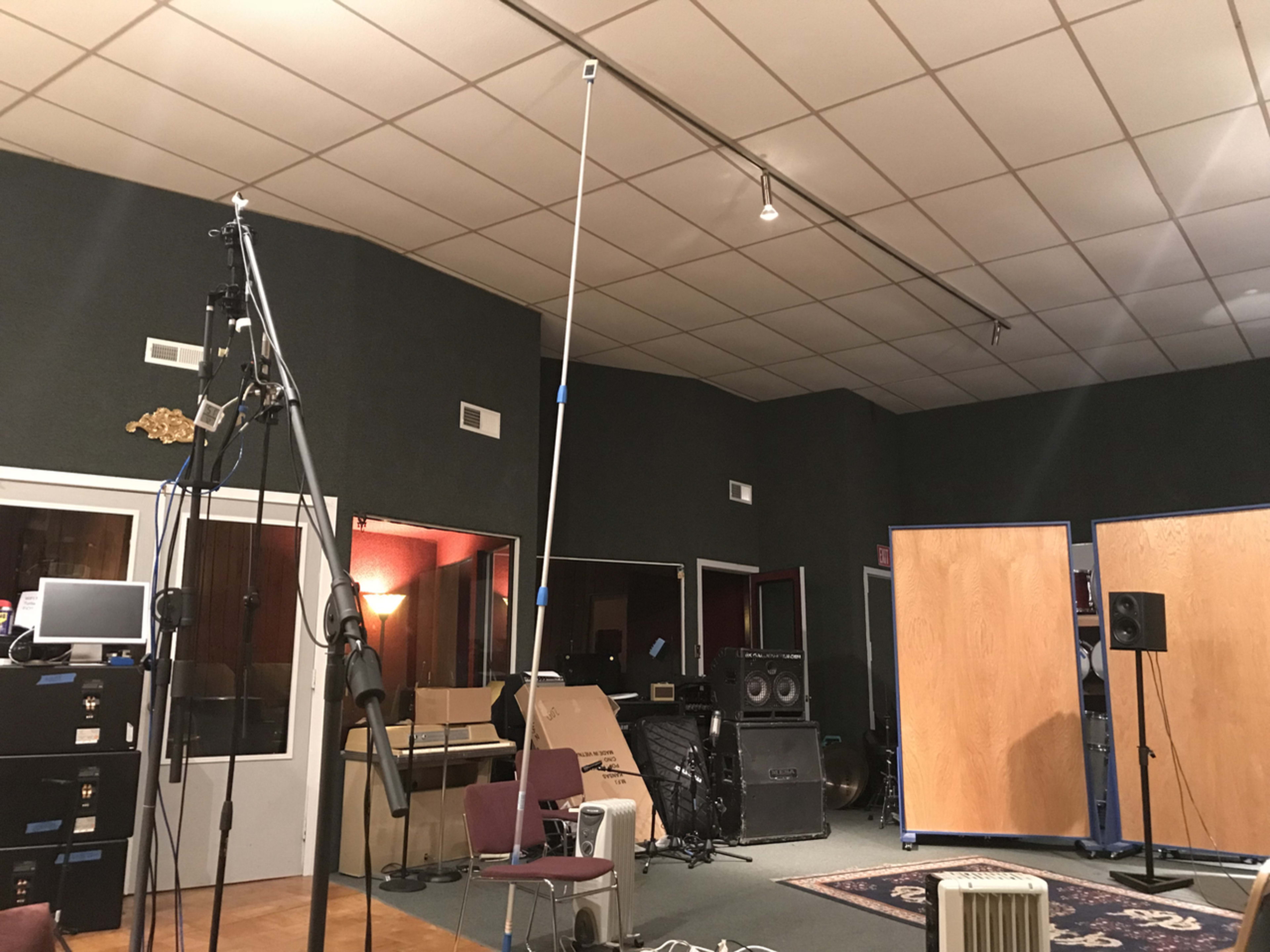 A recording studio with various equipment, including microphones on stands and soundproofing panels against the walls.