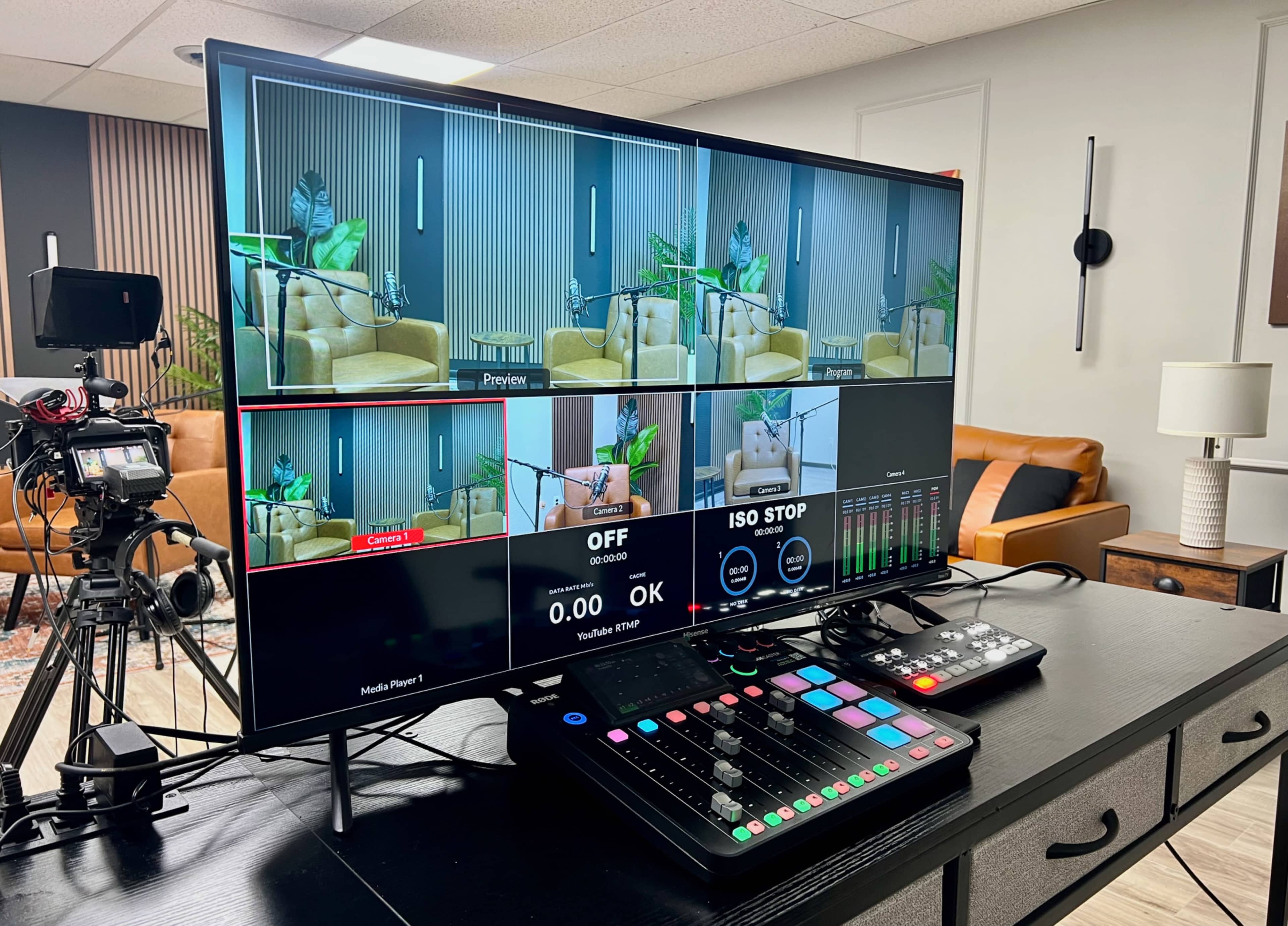 The image shows a control room setup with a large monitor displaying multiple camera feeds and a control panel with various buttons and sliders, all situated in a modern office environment.