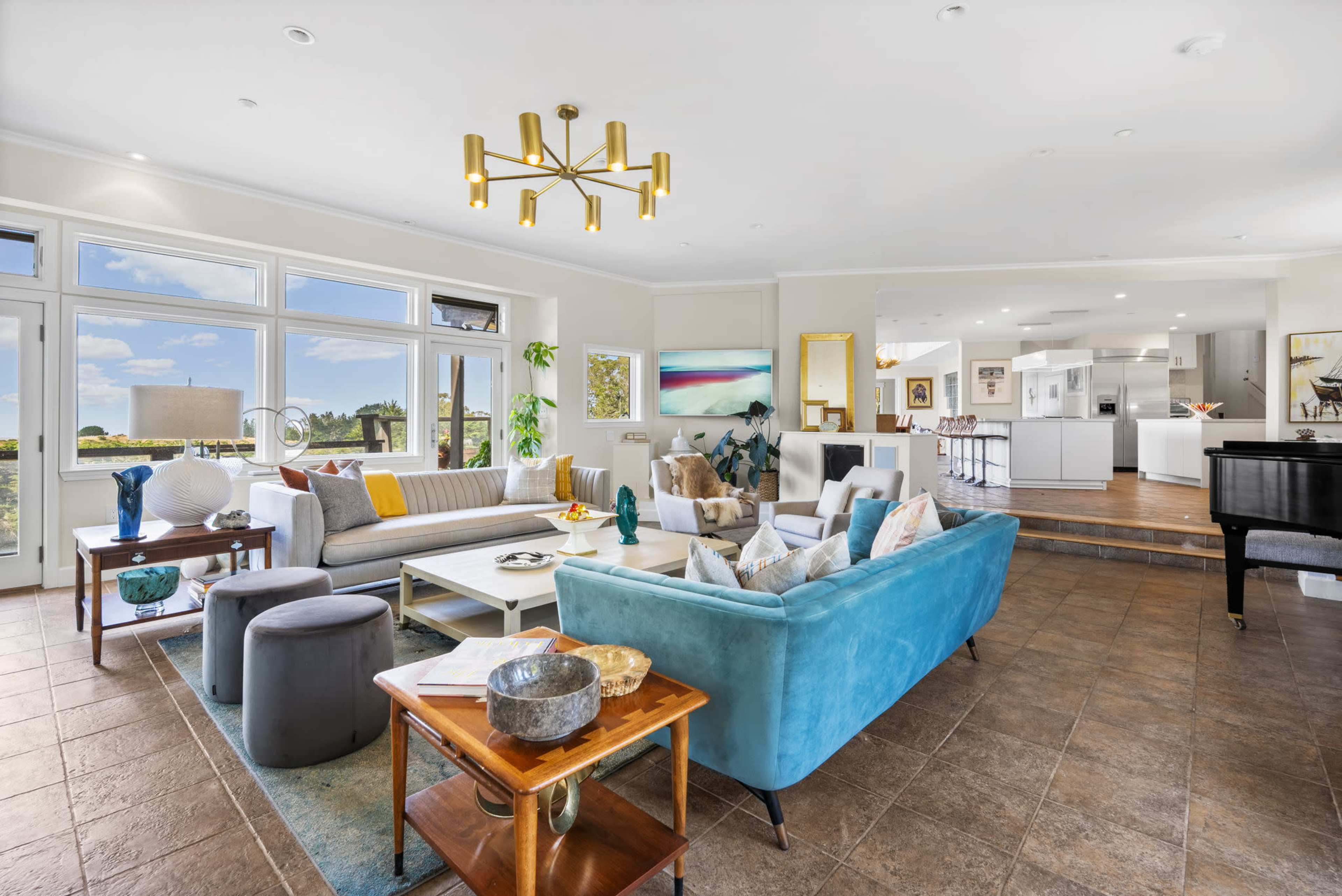 A spacious living room features various seating arrangements, a large window with a view, and an adjoining kitchen area.